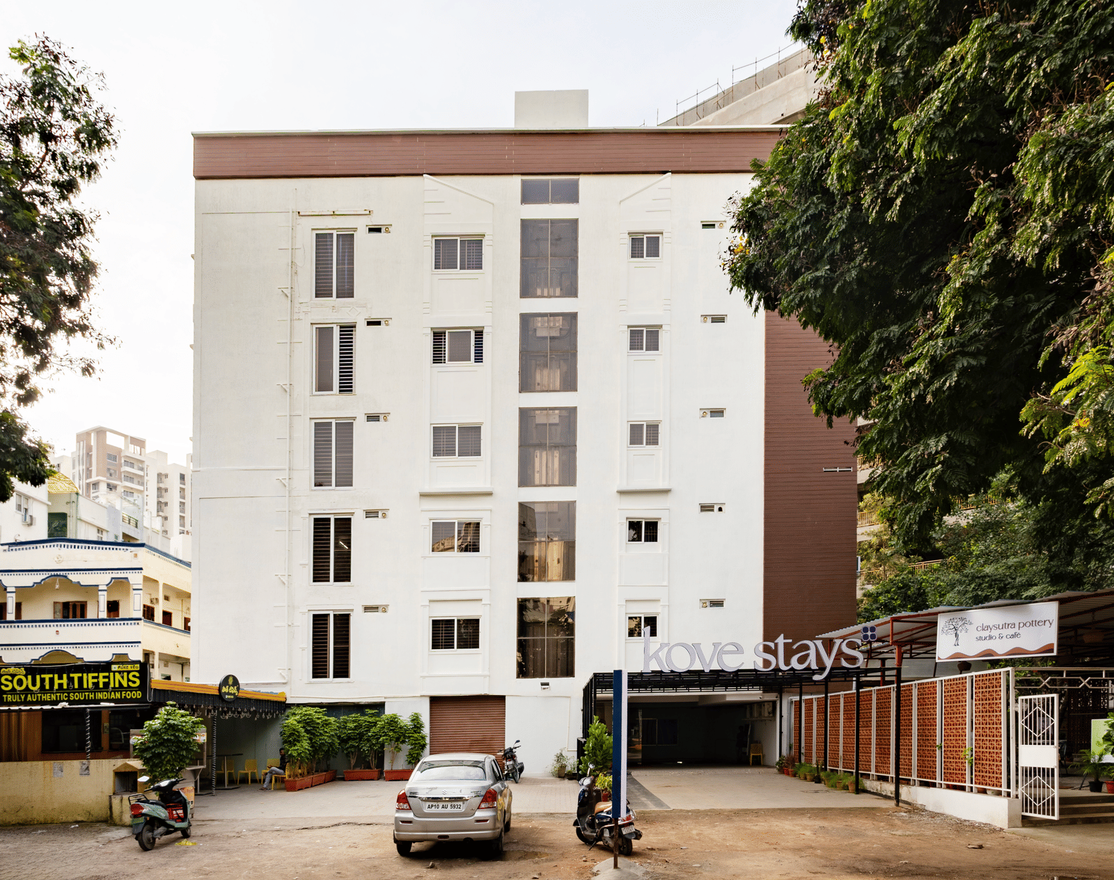 The multi-storey apartment building of Kove Smart Stays, with an underground parking entrance visible from the street, with a few vehicles parked in front.