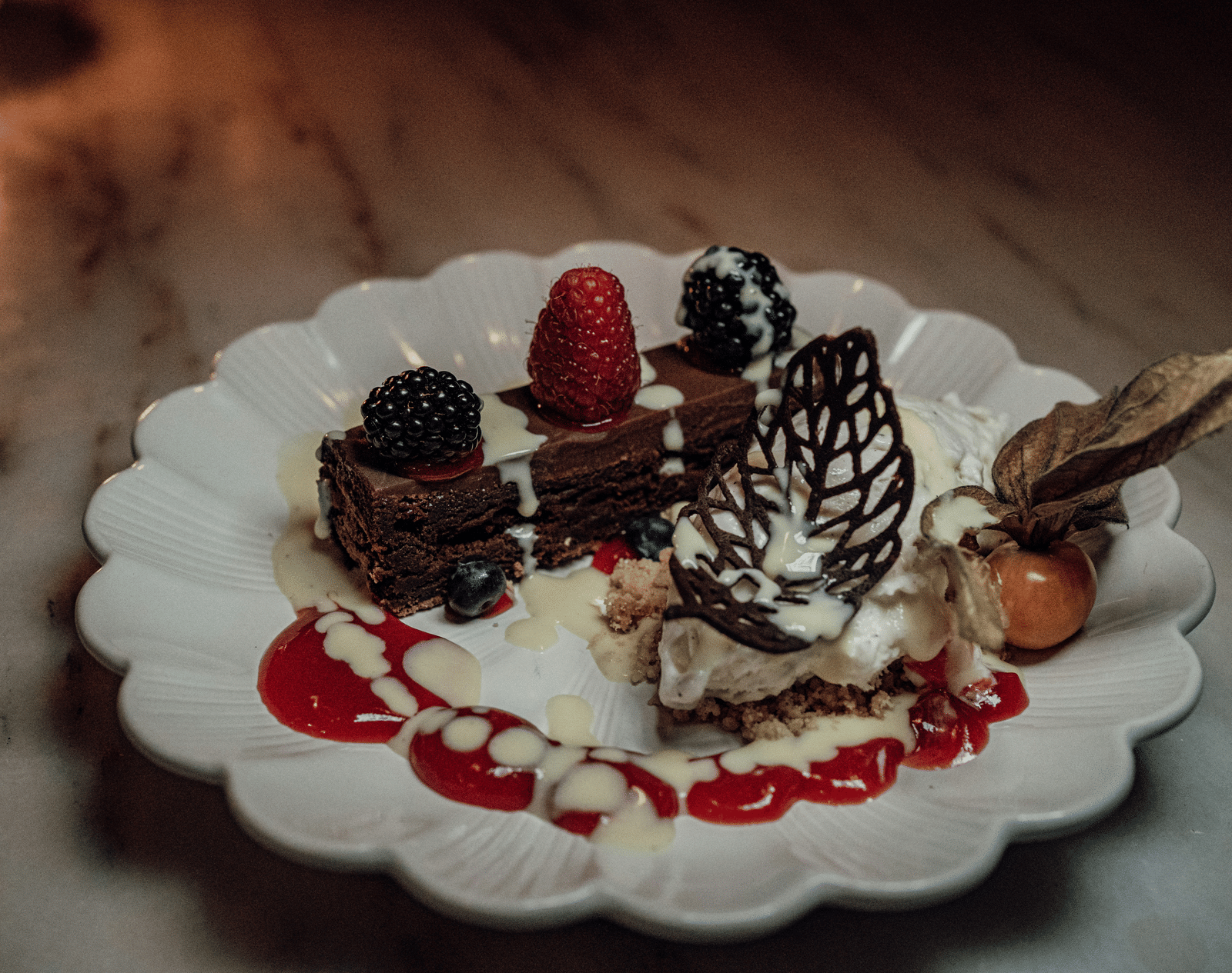 An artfully plated chocolate dessert with berries, cream, and a decorative chocolate lattice, served on a scalloped white plate.