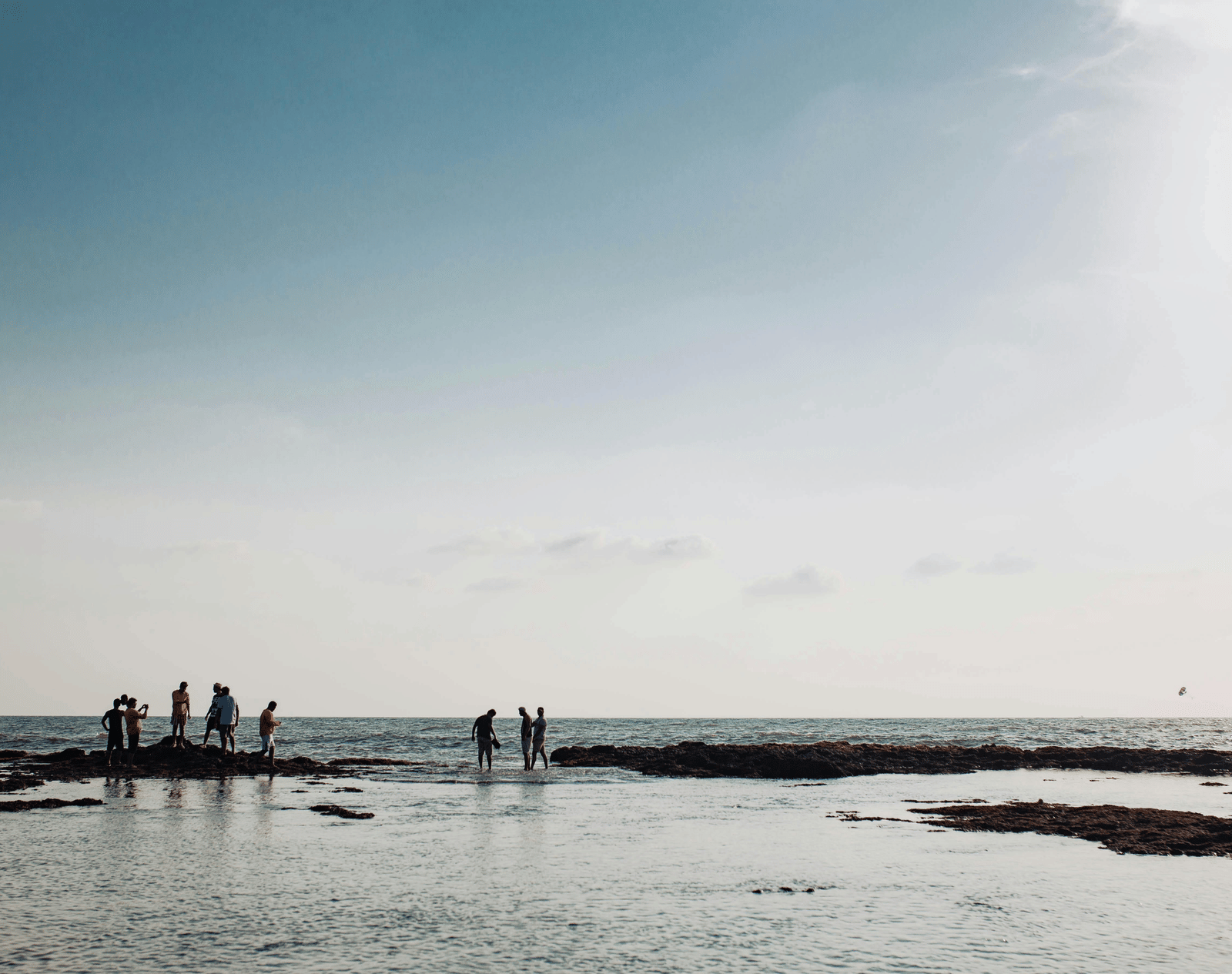 A group of people standing along a vast, shallow tidal beach under a hazy bright sky.