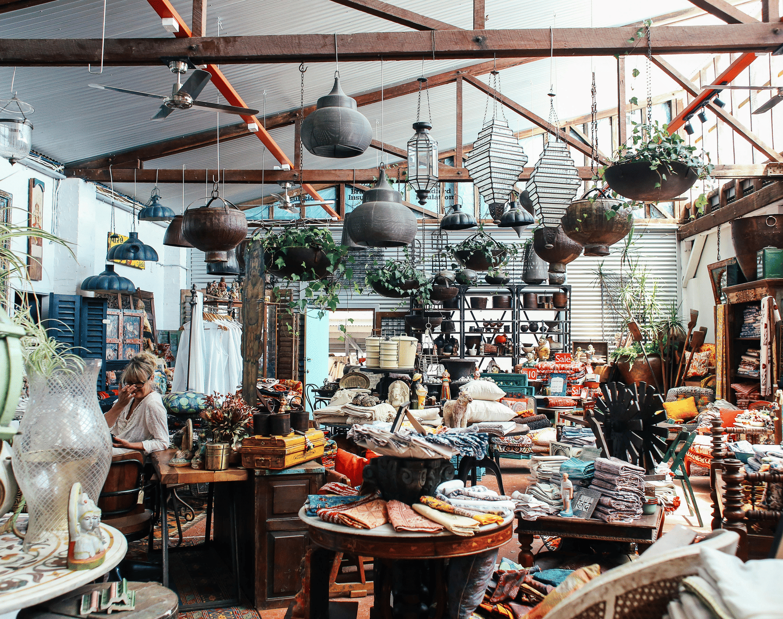A bustling antique market filled with vintage items, crockery, and hanging lights.