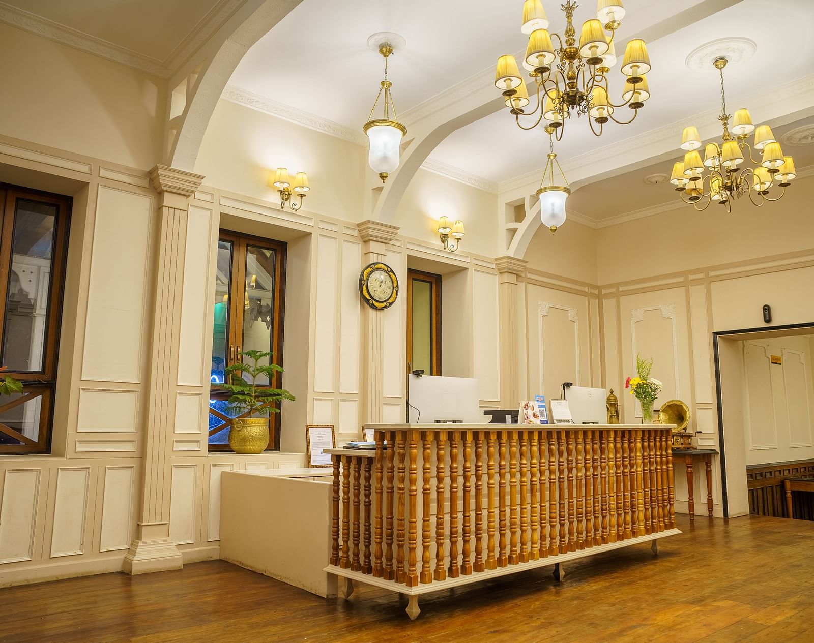 A warmly lit reception area  of Orisino Hotel & Spa that features a wooden front desk, ornate chandeliers, and large windows