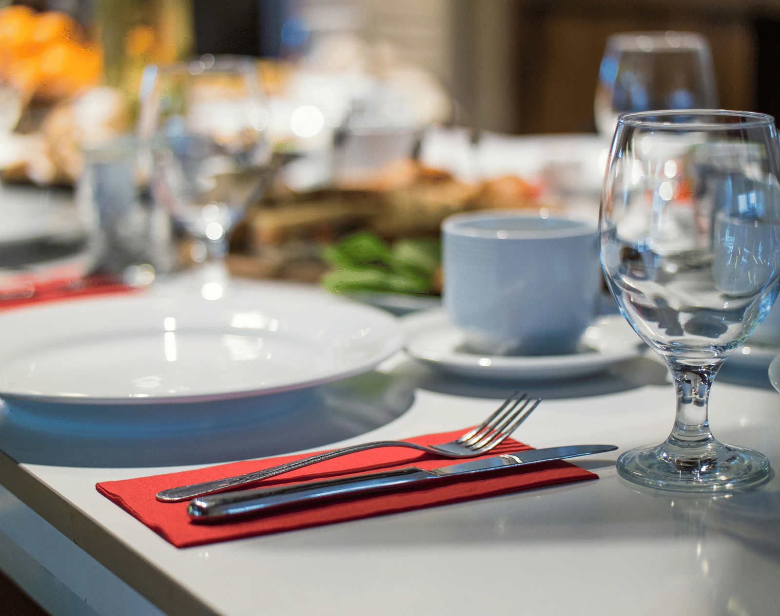 A table is elegantly set for a meal with a white plate, wine glass, and red napkin in a restaurant.