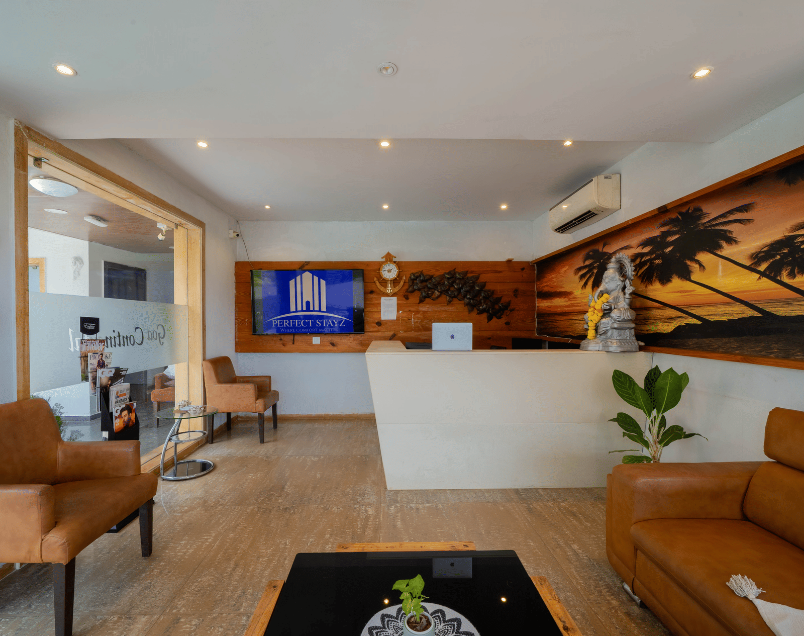 A stylish hotel reception area with a counter, comfortable leather seating, and a decorative beach mural - Perfectstayz Premium Goa Continental