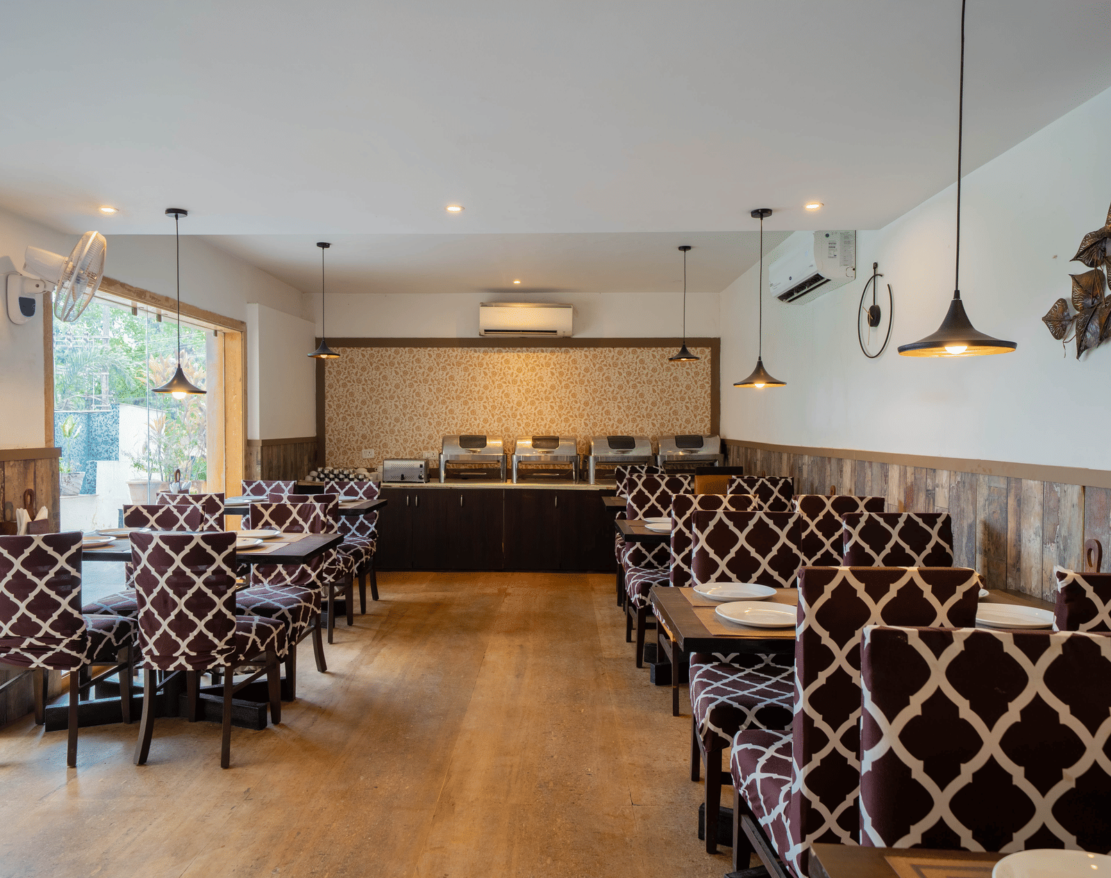 A well-lit, modern dining room featuring a patterned booth seating and wooden flooring at Perfectstayz Premium Goa Continental.
