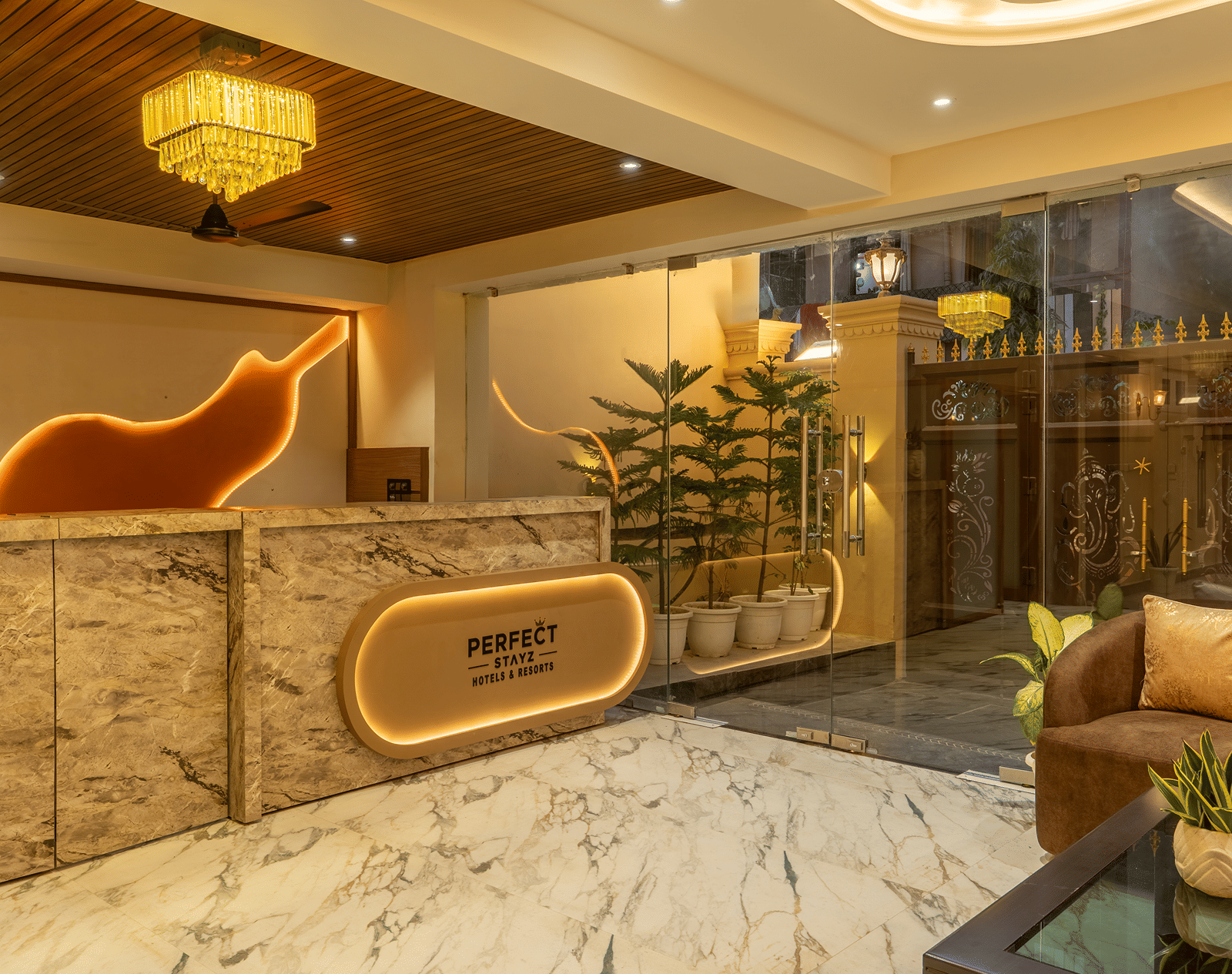 Reception at Perfectstayz Premium Lavender, Varanasi with a marble front desk, backlit Perfect Stayz sign, orange wall feature, and chandelier.