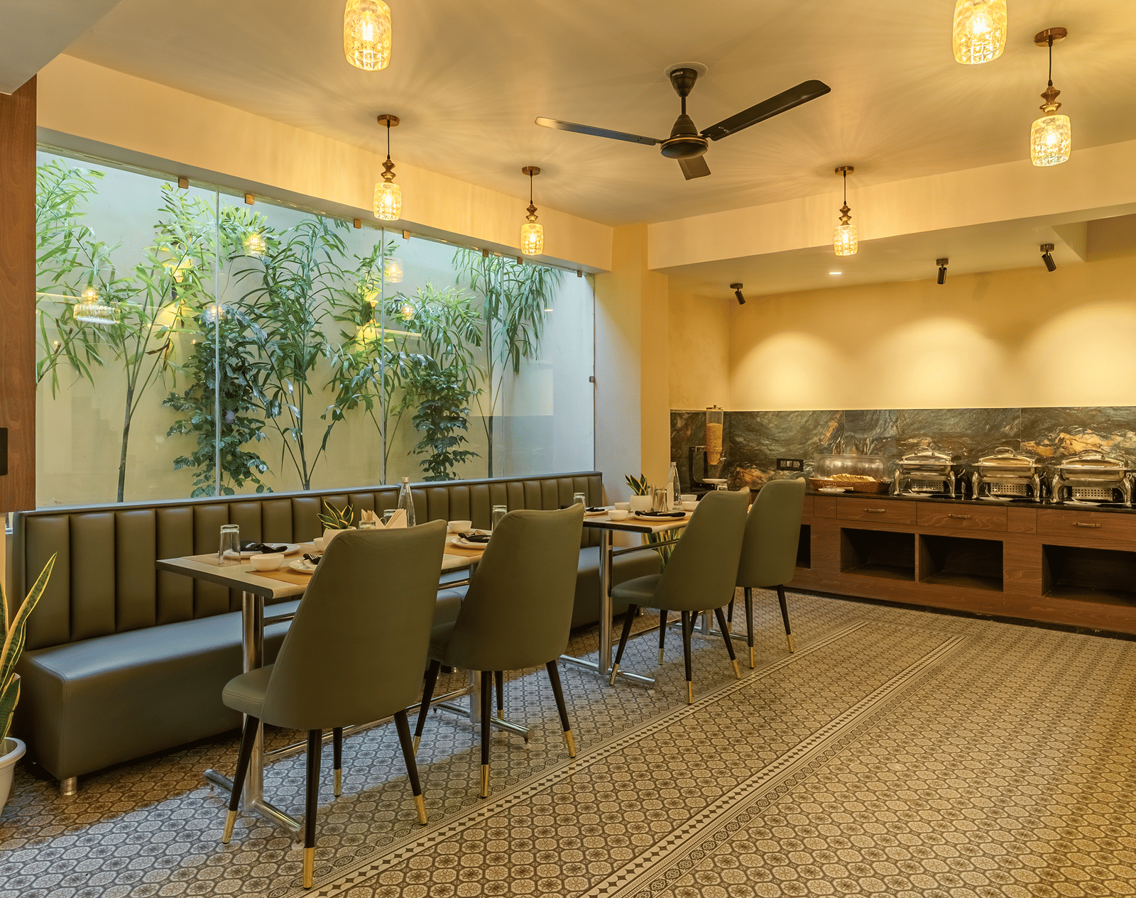 Wide view of the restaurant at Perfectstayz Premium Lavender, Varanasi with green chairs, a banquette, patterned floor tiles, pendant lamps, and a buffet counter.