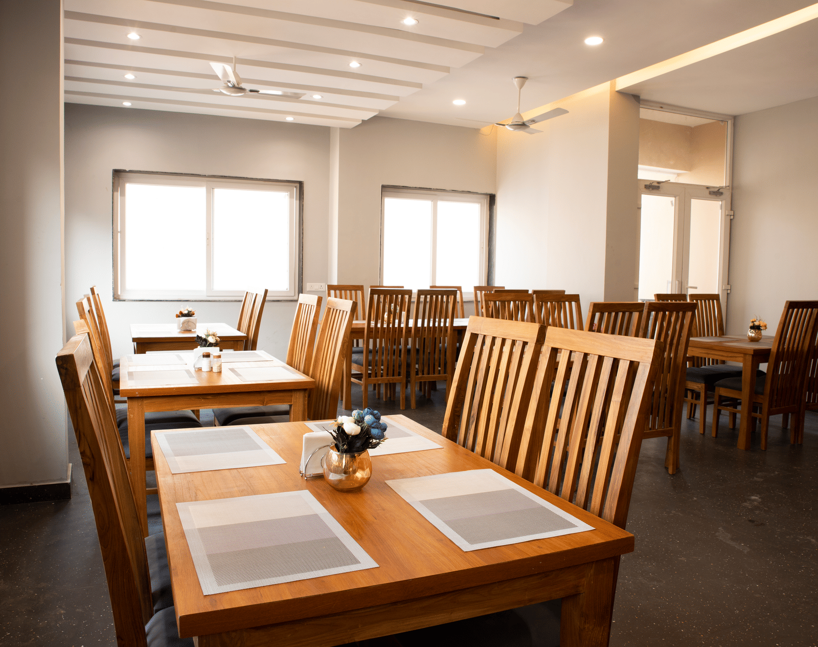 A dining area with wooden dining tables, place mats and chairs set neatly in a well-lit room at Perfectstayz Premium Laxmi Heritage, Rishikesh.