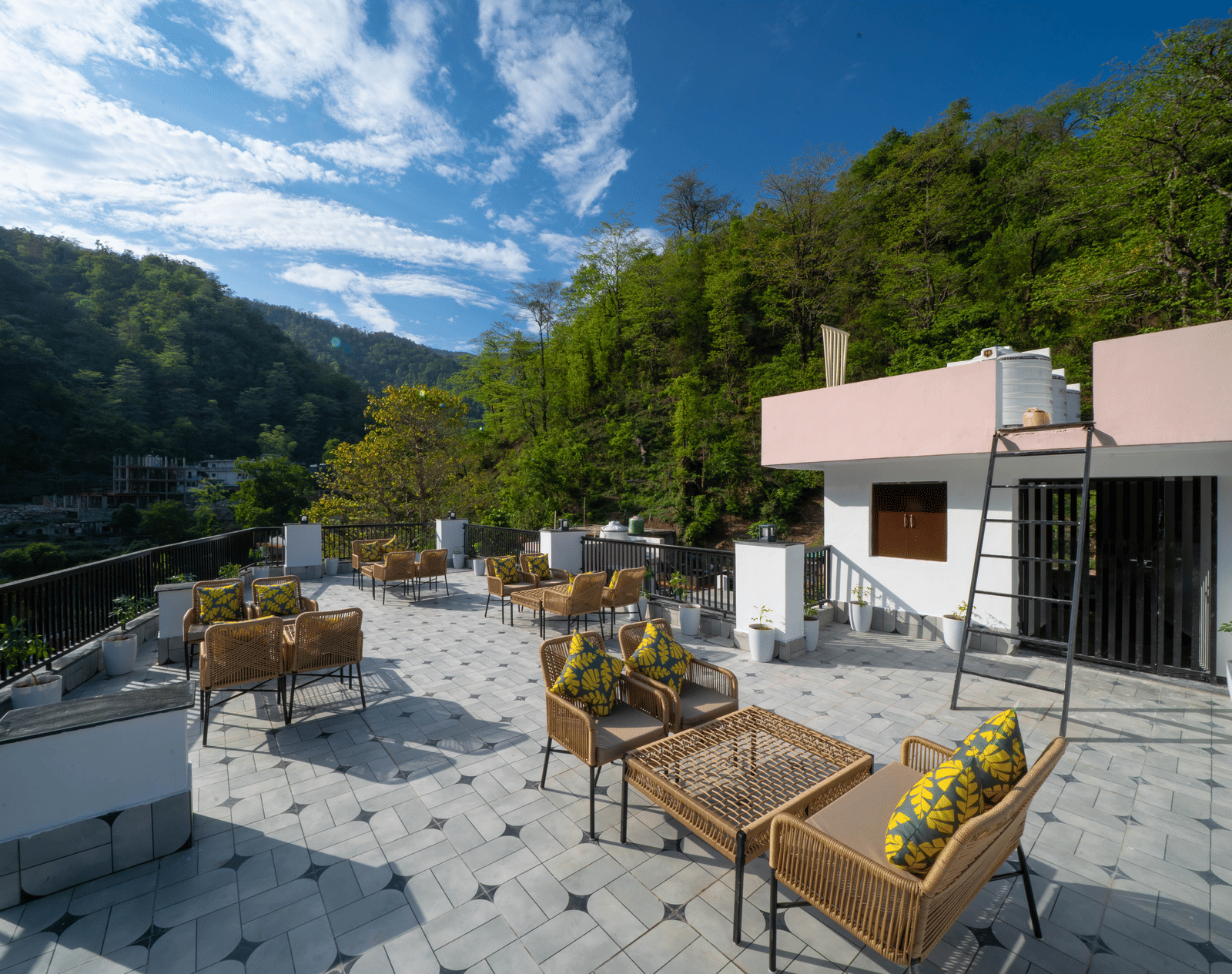 A rooftop terrace with tables, chairs, floor tiles, and a building structure with a flat roof in Perfectstayz Premium Mystic Falls, Rishikesh.