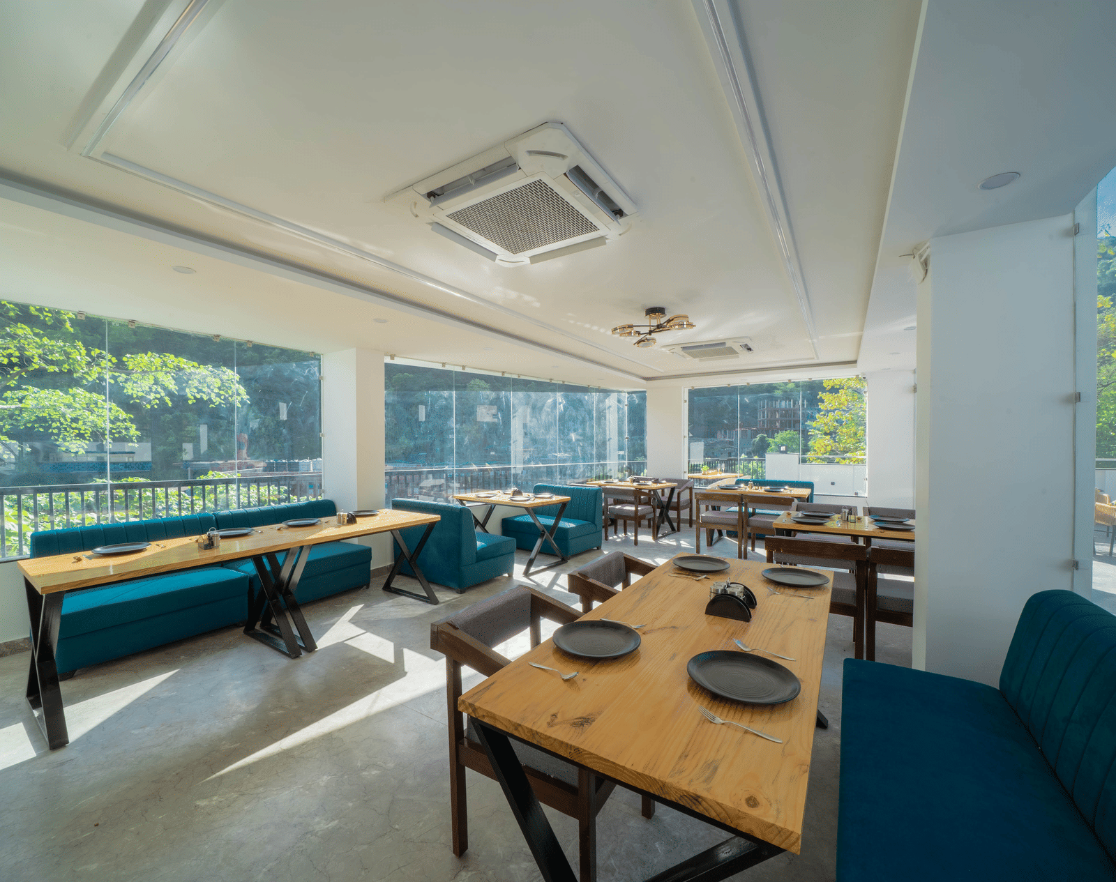 An indoor dining area with tables, benches, chairs, plates set on the tables, and a window view of trees outside in Perfectstayz Premium Mystic Falls, Rishikesh.