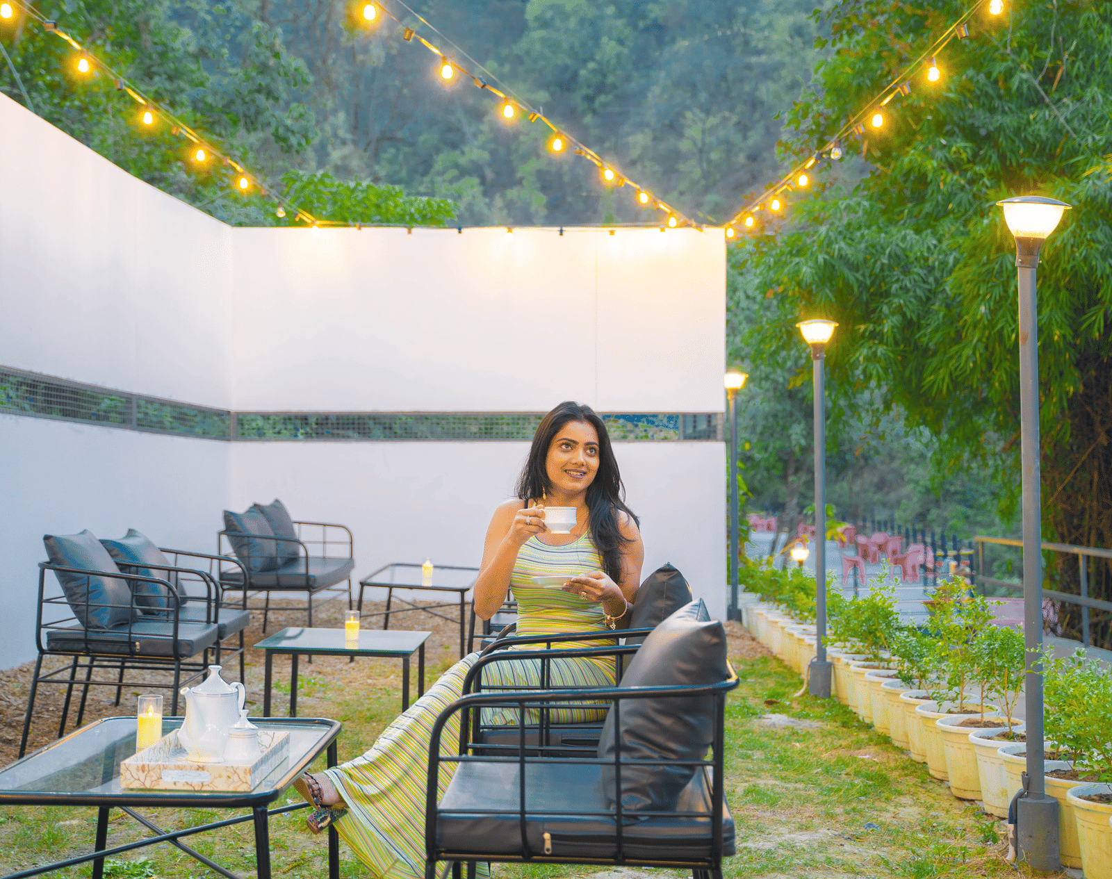 A person sits at an outdoor table at Perfect Stayz The Jungle Resort under string lights.