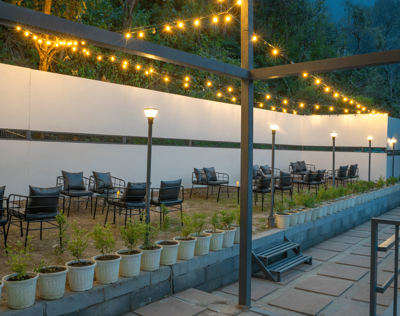 An outdoor dining area at Perfect Stayz The Jungle Resort is lit by string lights over tables and chairs.