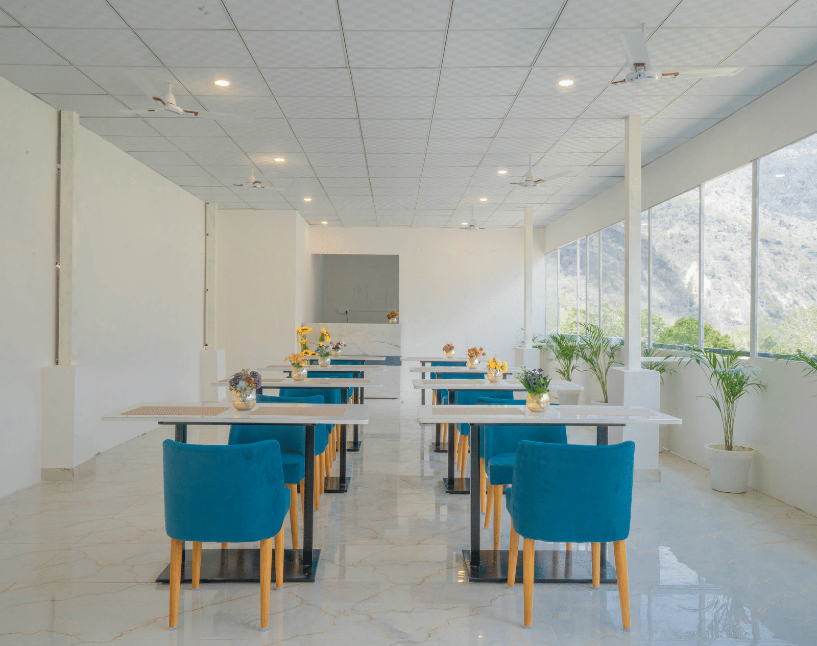 A spacious dining hall at Perfectstayz Value Alpine Retreat, Rishikesh with white interiors and neatly arranged chairs and tables.