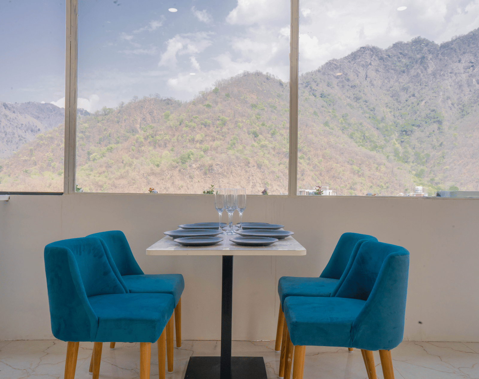 A dining area at Perfectstayz Value Alpine Retreat, Rishikesh with large windows offering beautiful views of the surrounding hills.