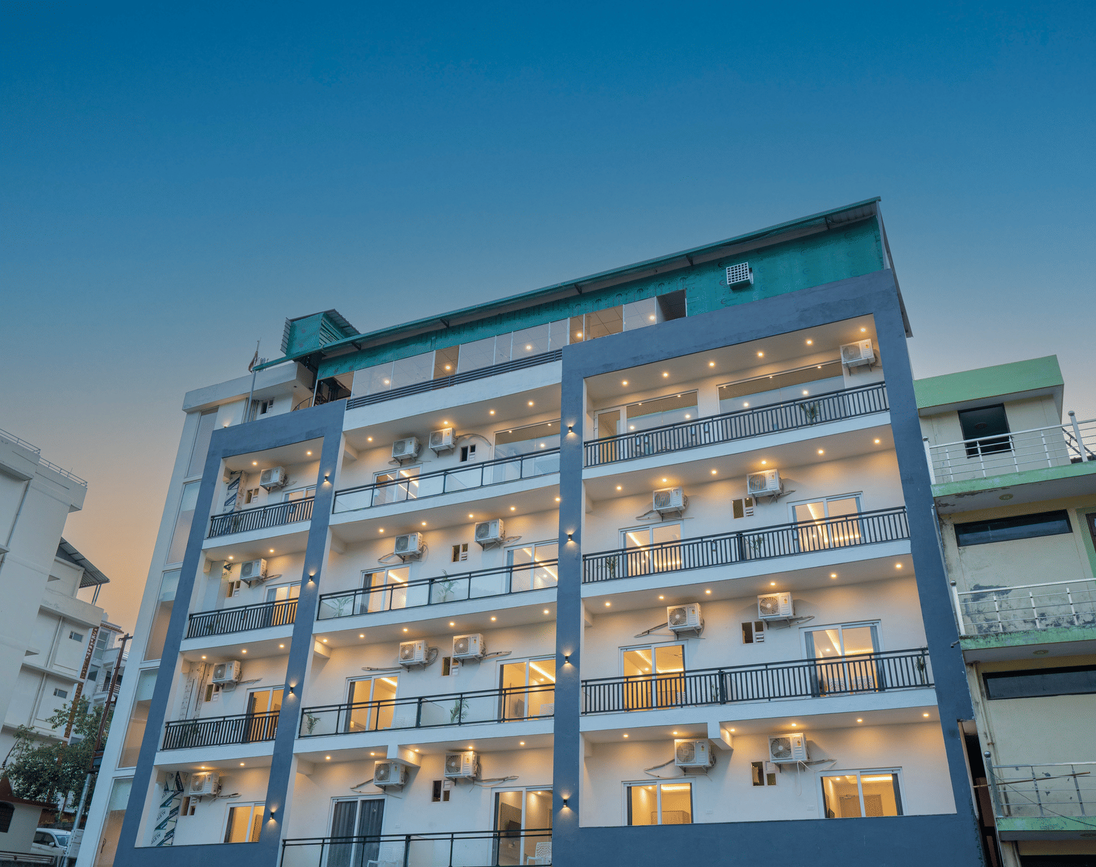 A modern building of Perfectstayz Value Alpine Retreat, Rishikesh with multiple balconies, against a clear blue sky.