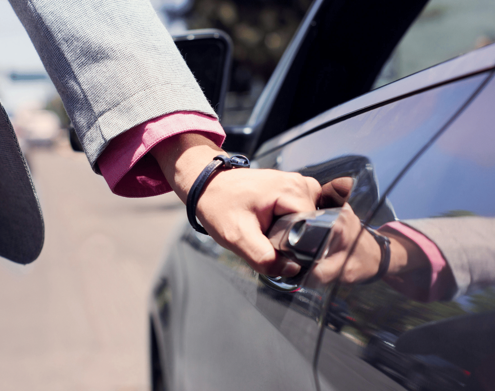 A person dressed in business formals opening the door of a car.