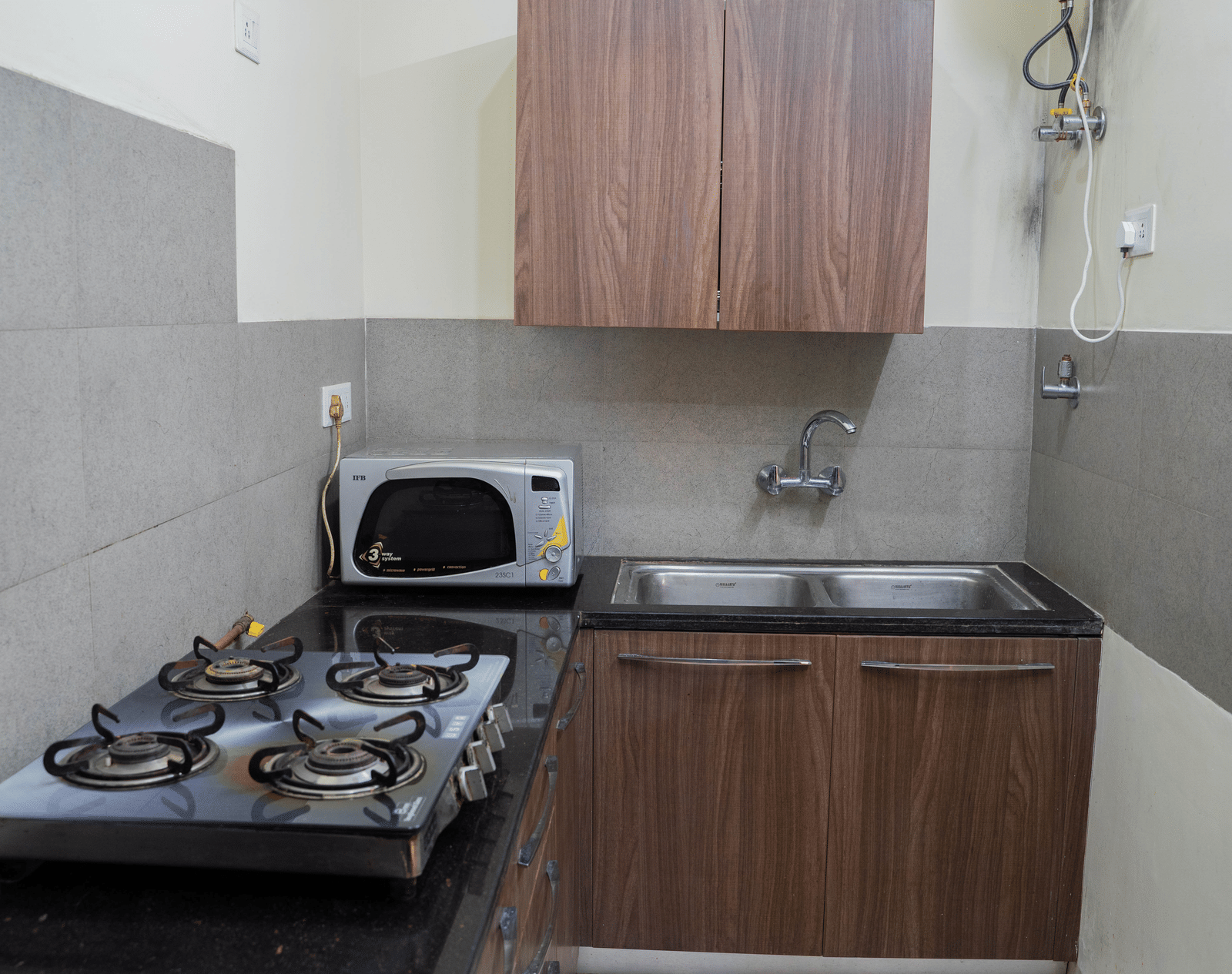 A kitchen area with a gas stove, microwave, sink, and wooden cabinets on a countertop against tiled walls at Perfectstayz Value Shimla (Namah Retreat).