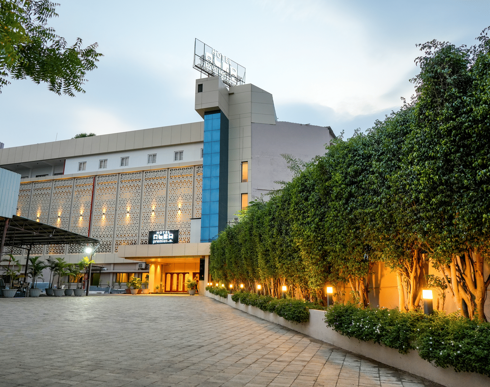 Exterior view of hotel building with driveway and trees at Pravasa Hotel, Kolhapur.