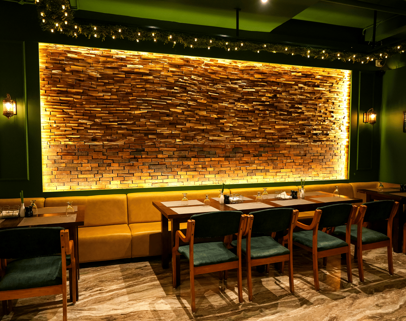  A warm dining section with a long yellow upholstered booth and a dramatic backlit stone feature wall at Pravasa Hotel, Kolhapur.