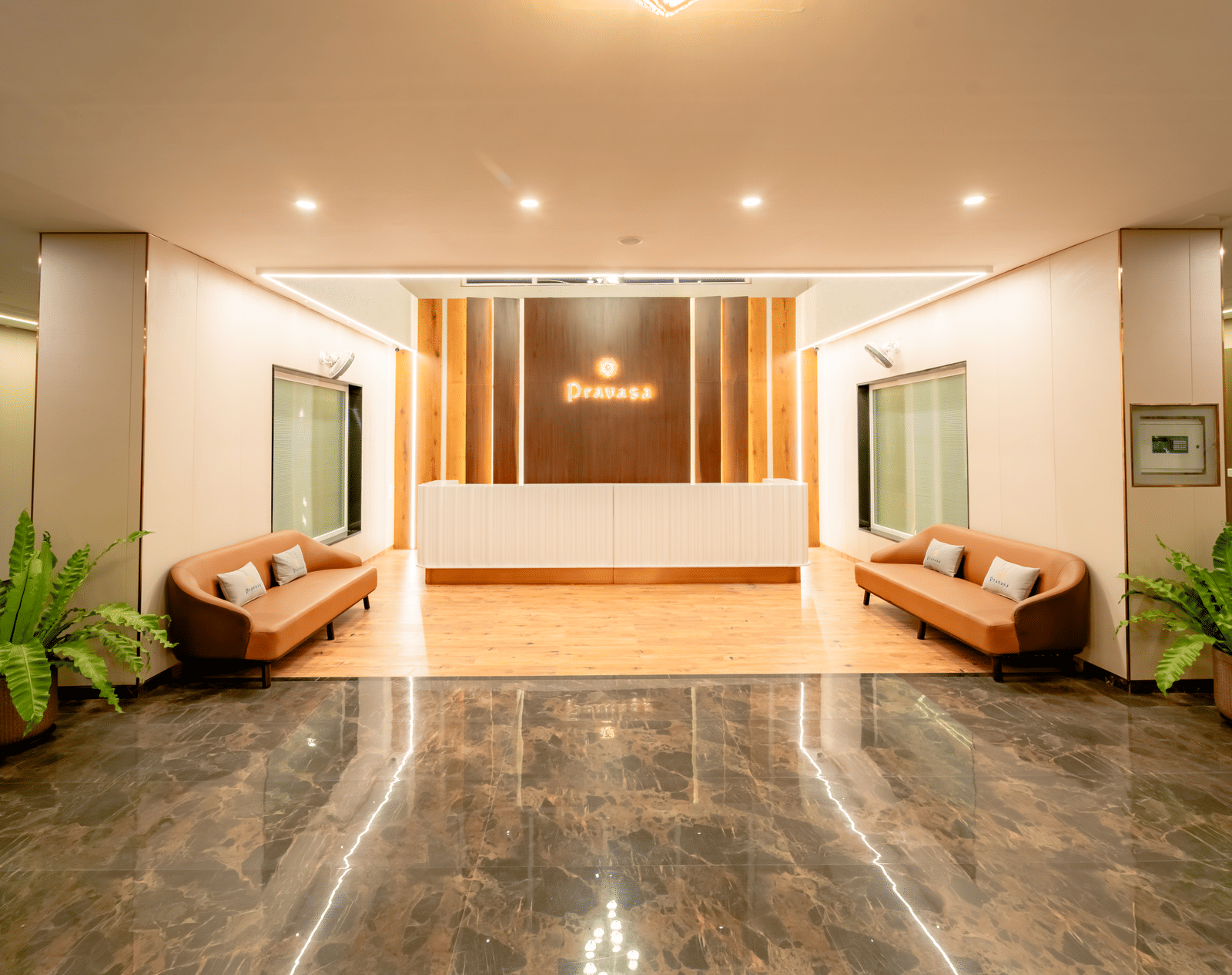 Reception area of the hotel with 2 sofas and potted plants | Pravasa Hotel, Vijayapura