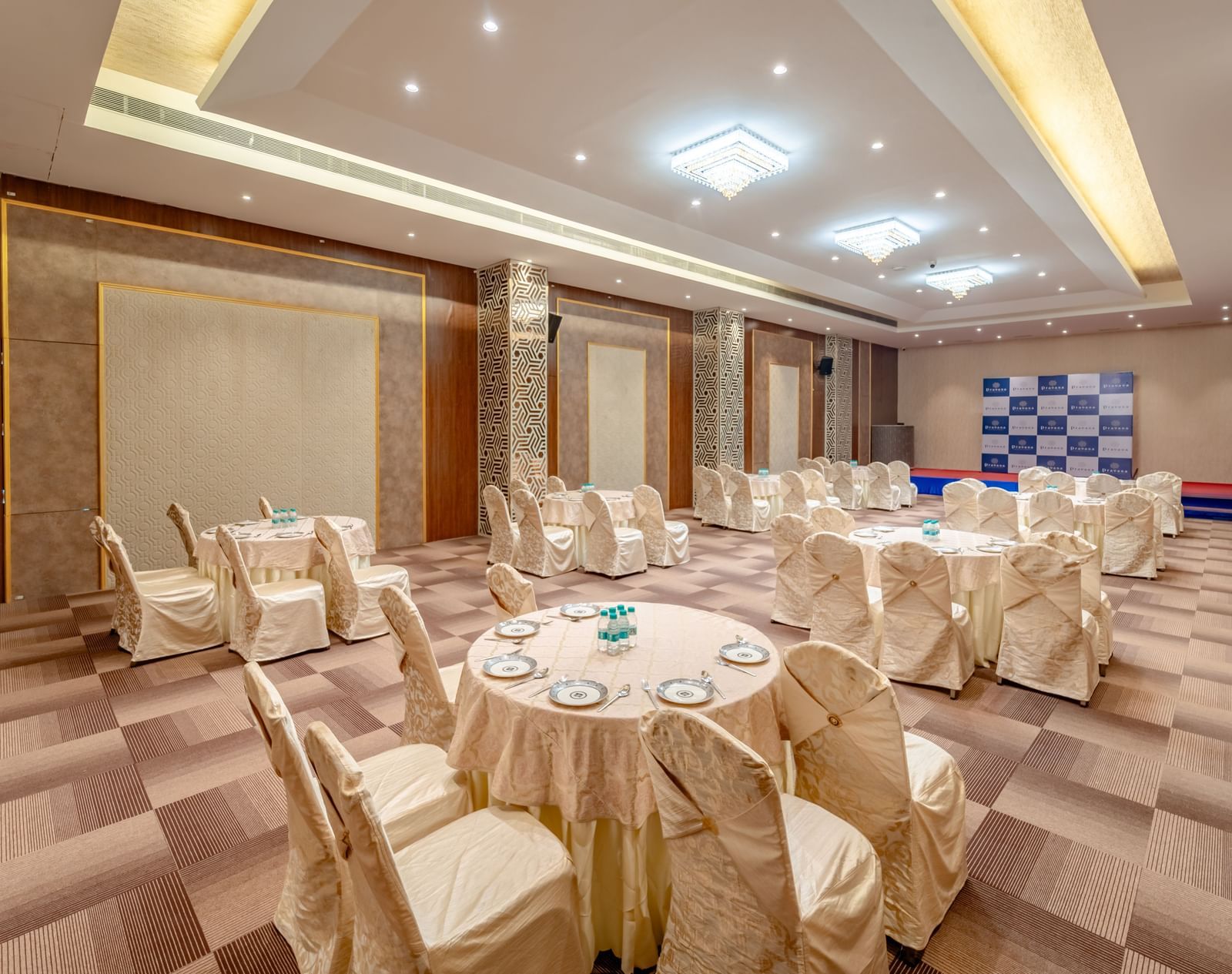 A banquet hall with round tables and beige chairs | Meetings & Events | Pravasa Hotel, Vijayapura