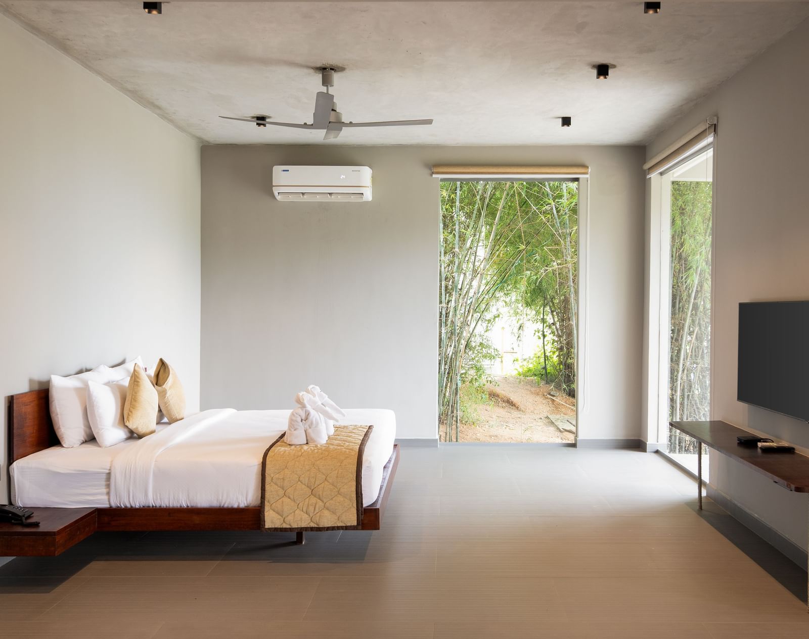 A minimalist bedroom with a large bed, a television, and an open doorway leading to an outdoor area | Gaia Studio | RD's Nature Retreat, Bangalore