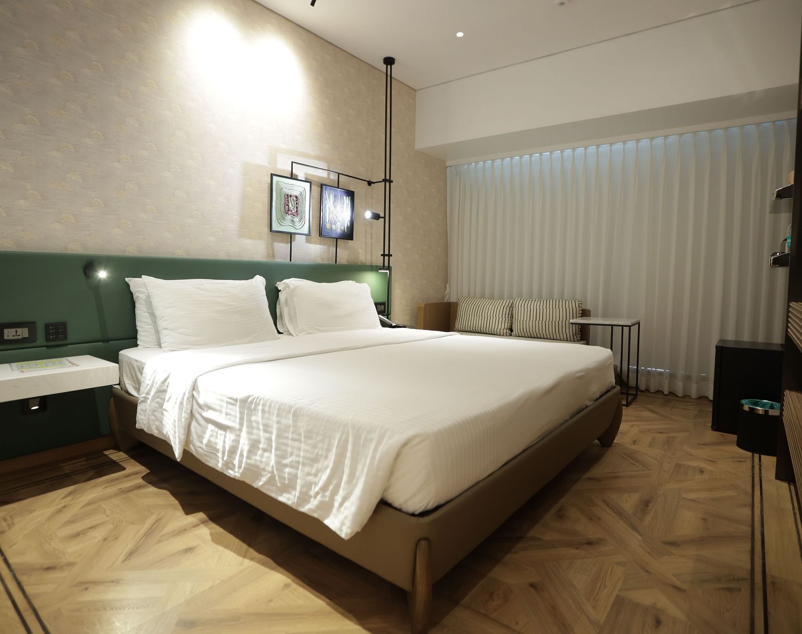 Modern guest room at Regency Hotel, Mumbai with plush bedding, contemporary furniture, large windows and elegant green accent wall for a comfortable stay.