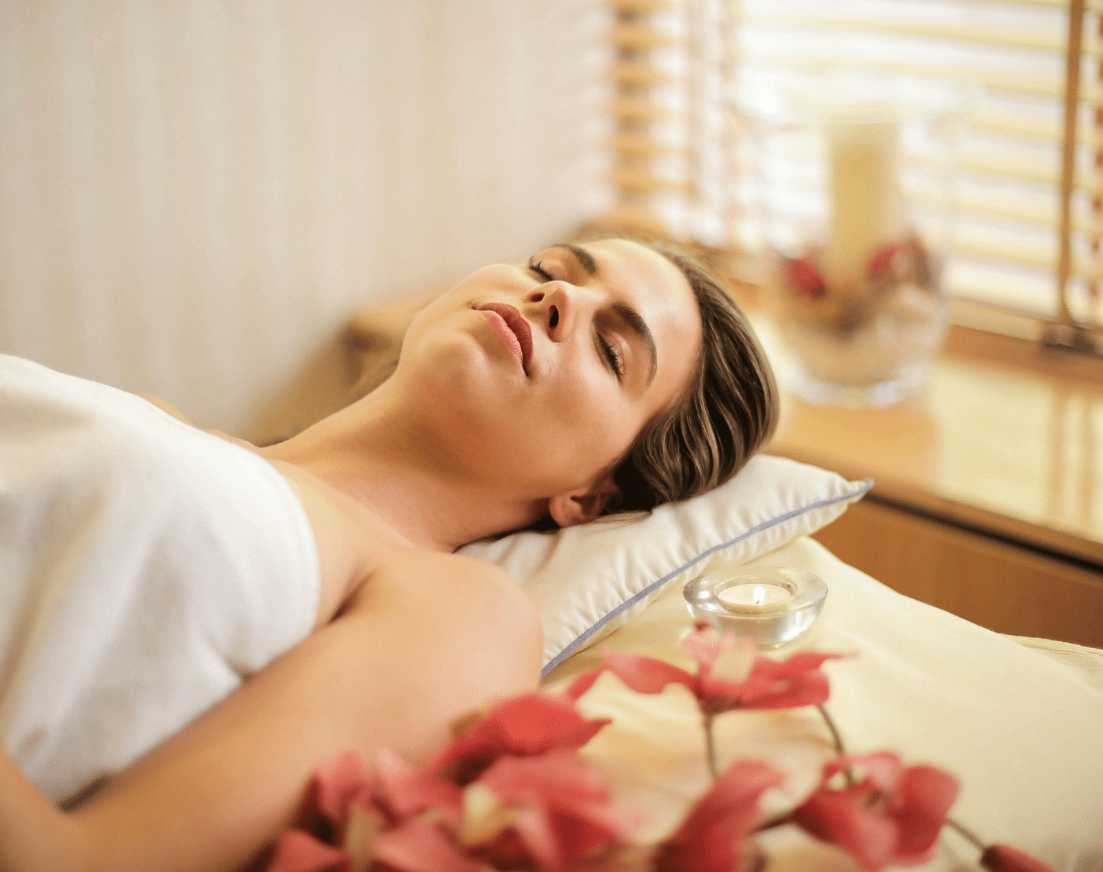 A woman lying down on a bed all relaxed in a brightly lit room.
