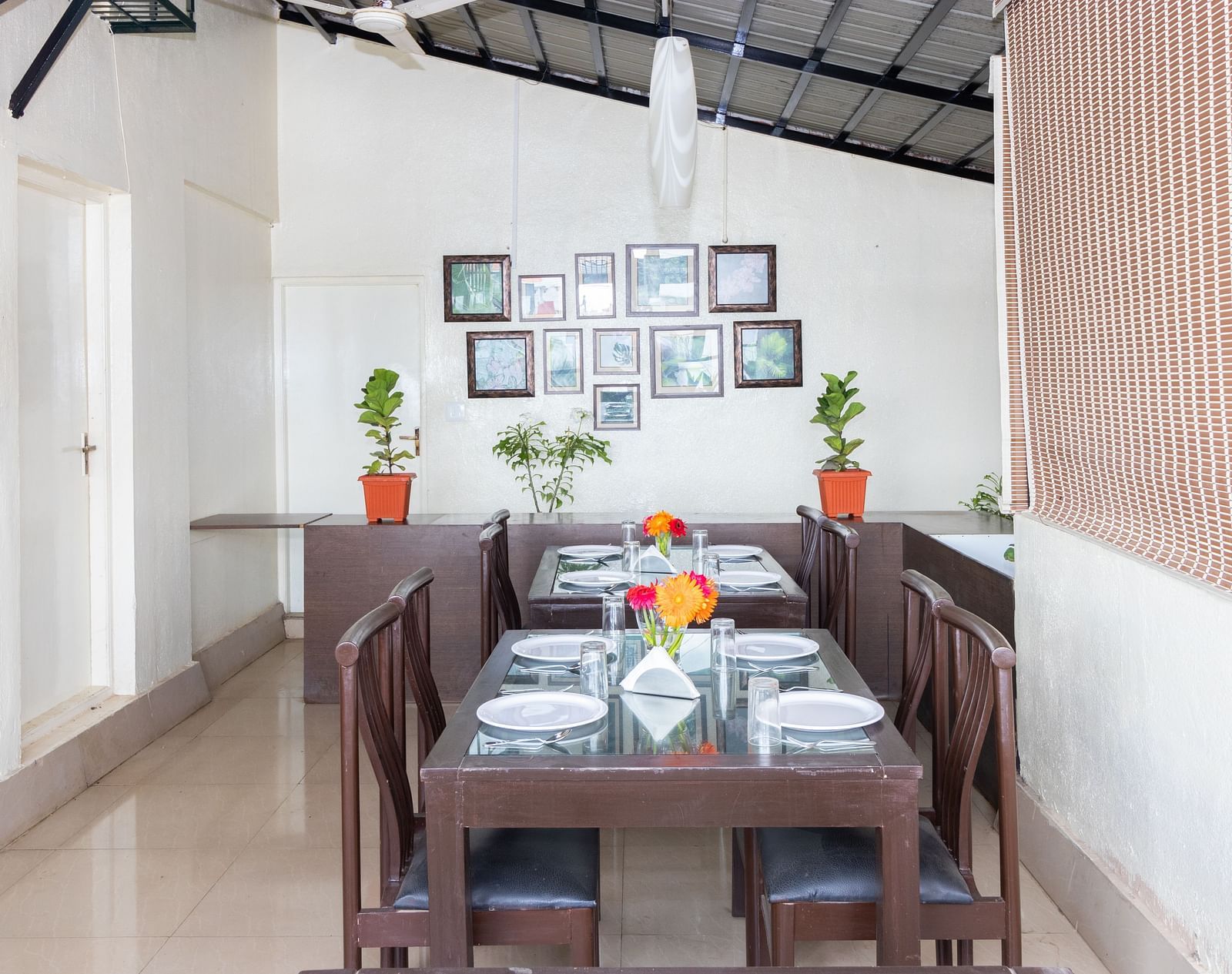 A dining area with a wooden table, chairs, and decorated with framed pictures and potted plants at Sanctum Suites Domlur, Bangalore.