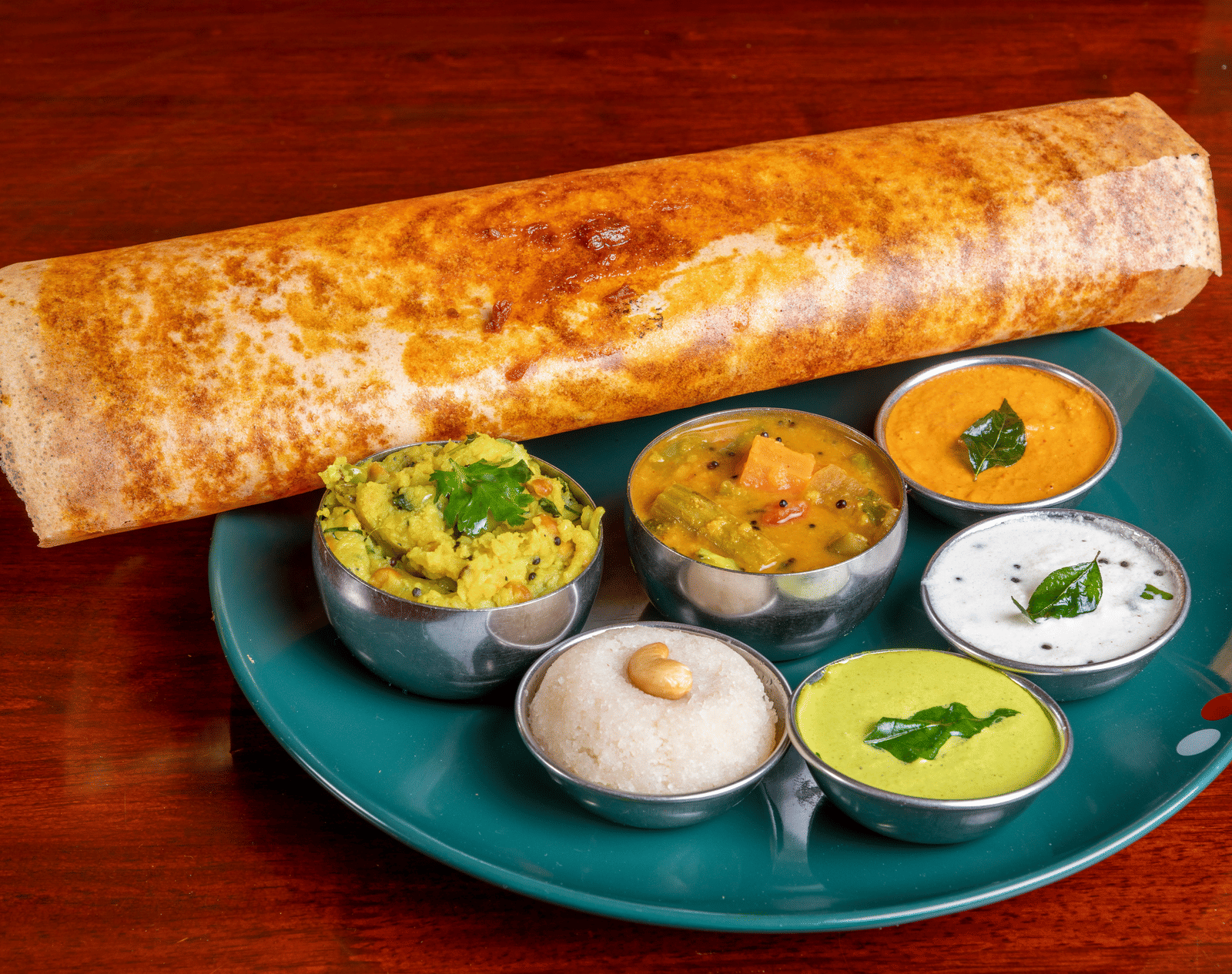 A long, golden-brown crispy dosa served on a plate with three different dipping chutneys.