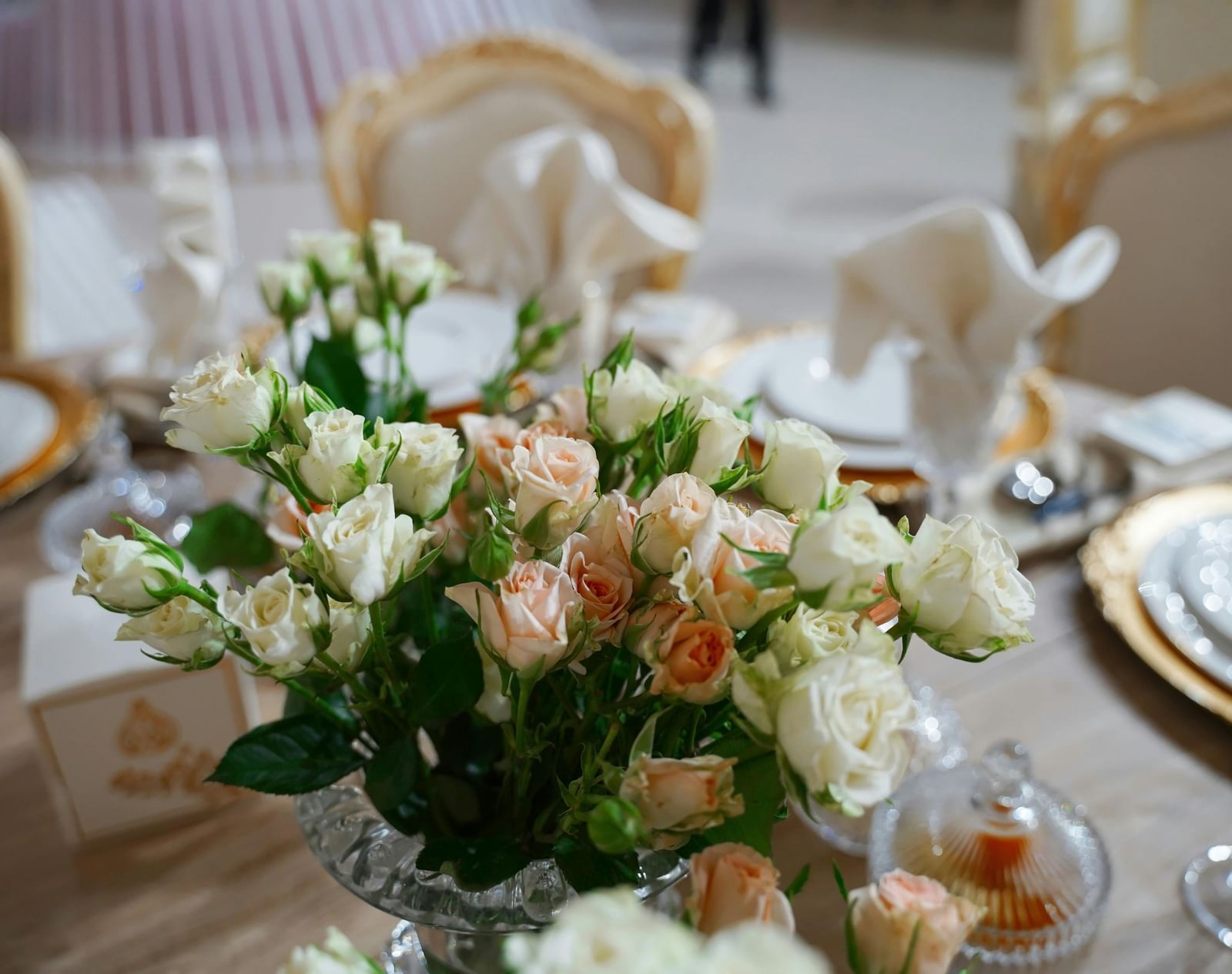 A close up shot of a beautiful flower vase with a lot of white and pink roses on a dining table. 
