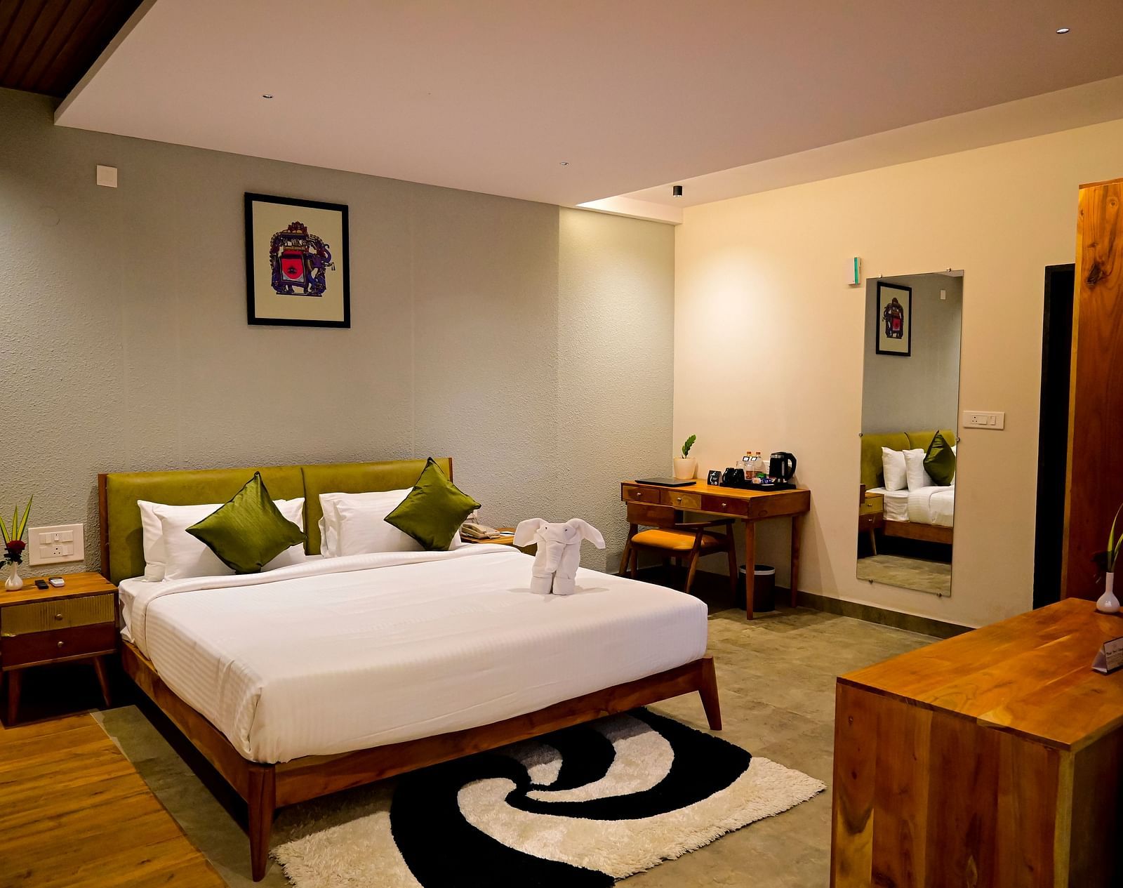 Hotel room with a large bed, olive green pillows, a unique black and white rug, and wooden furniture at TGI Livancia Hillside, JC Nagar, Mysore