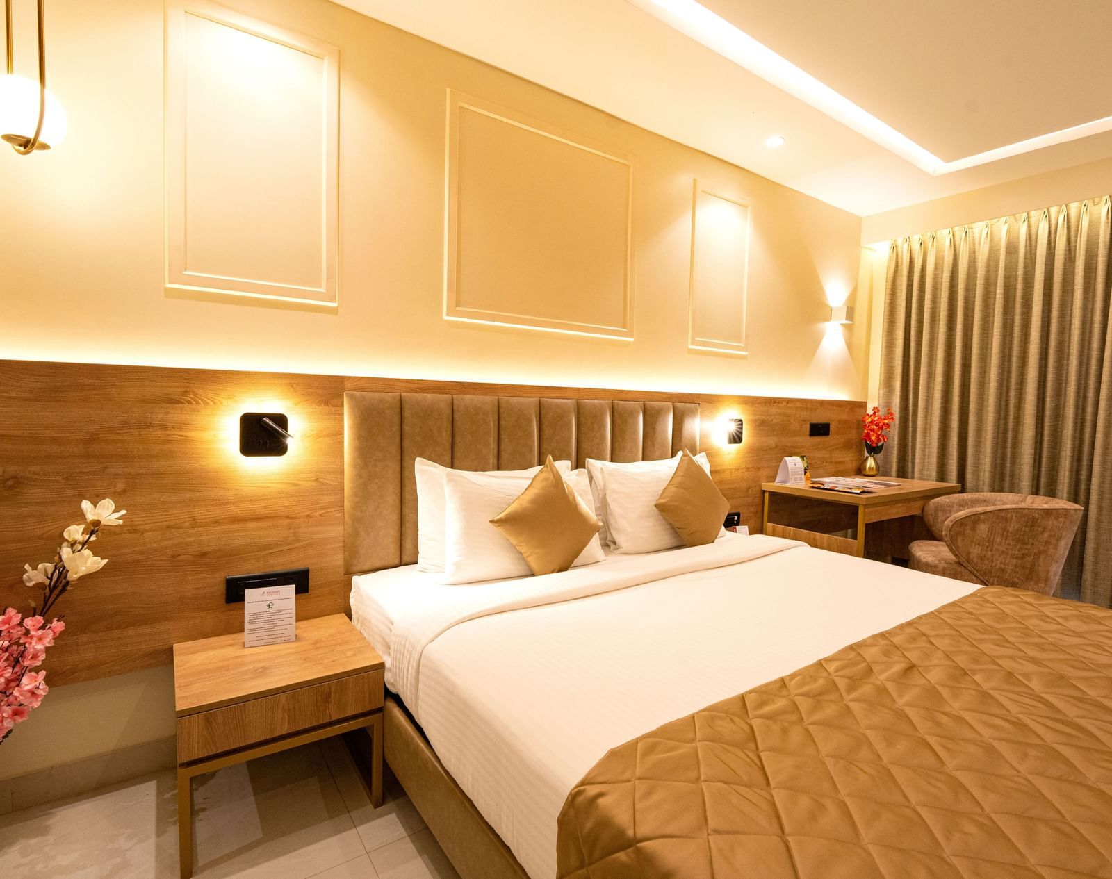Well lit bedroom with a king bed, side table, flower vase with pink flowers and curtained windows at TGI Star Holiday Resort.