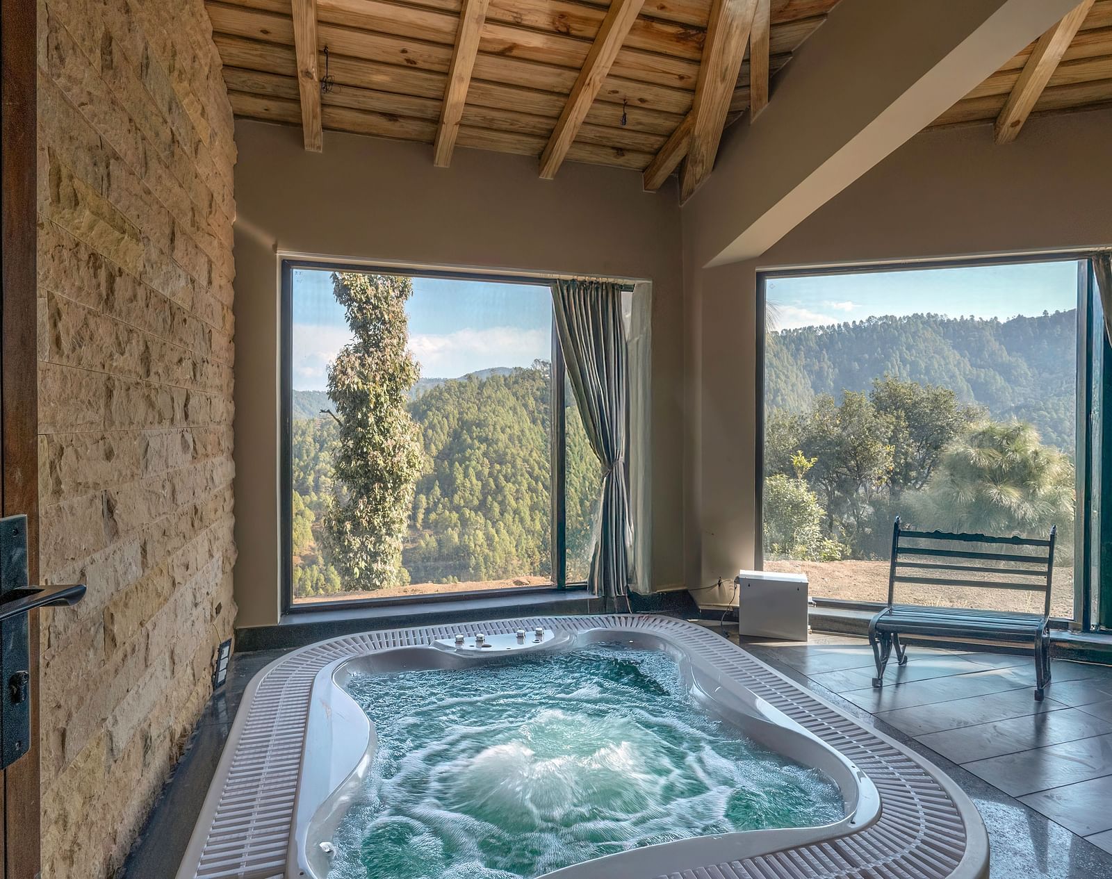 Spacious room with a Jacuzzi placed beside the wall and a seating area to the side, next to large windows with curtains pulled to the side at The Chamomile Estate.