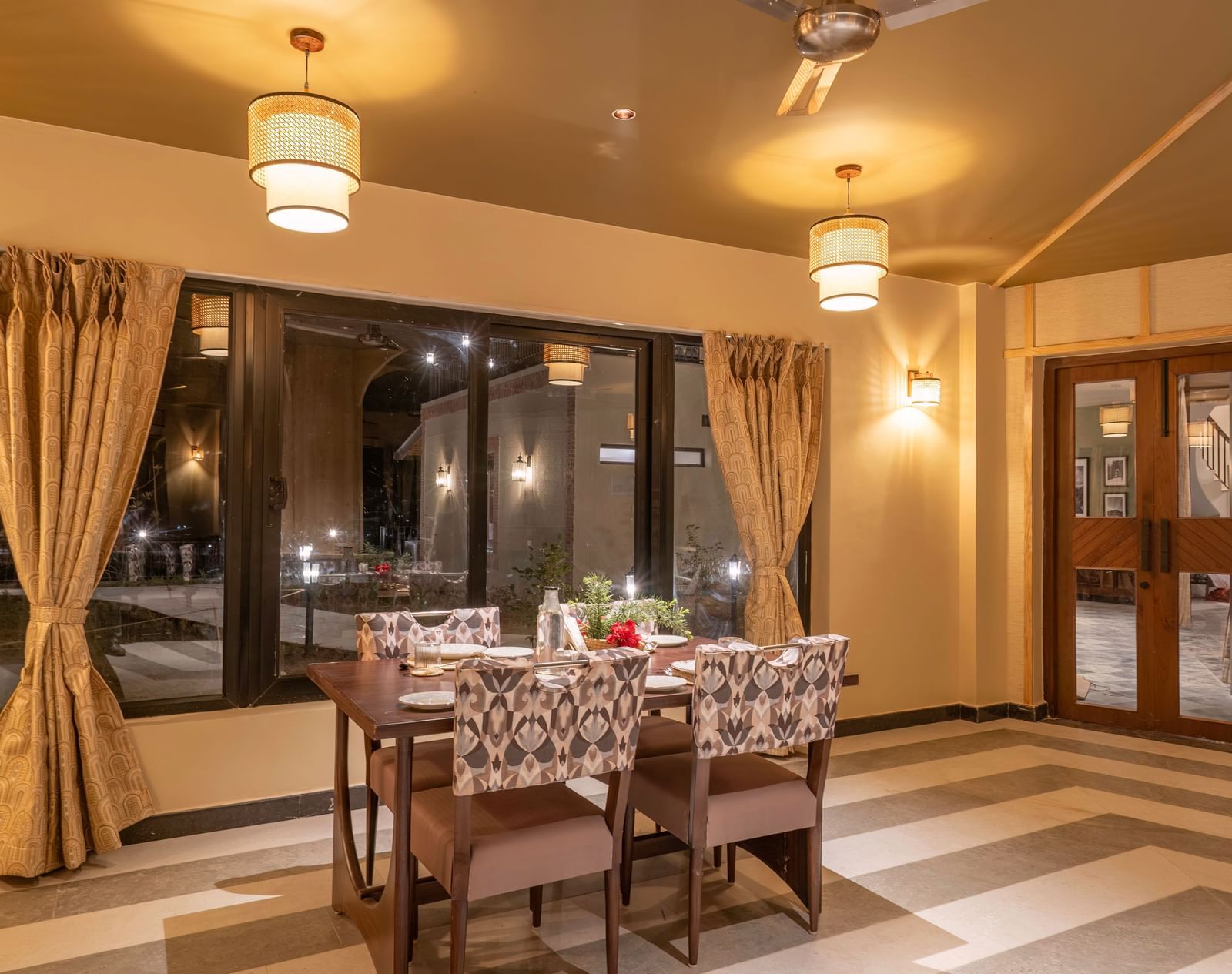 Elegant dining room with warm lighting, wooden furniture, and large curtained windows at The chamomile Estate.