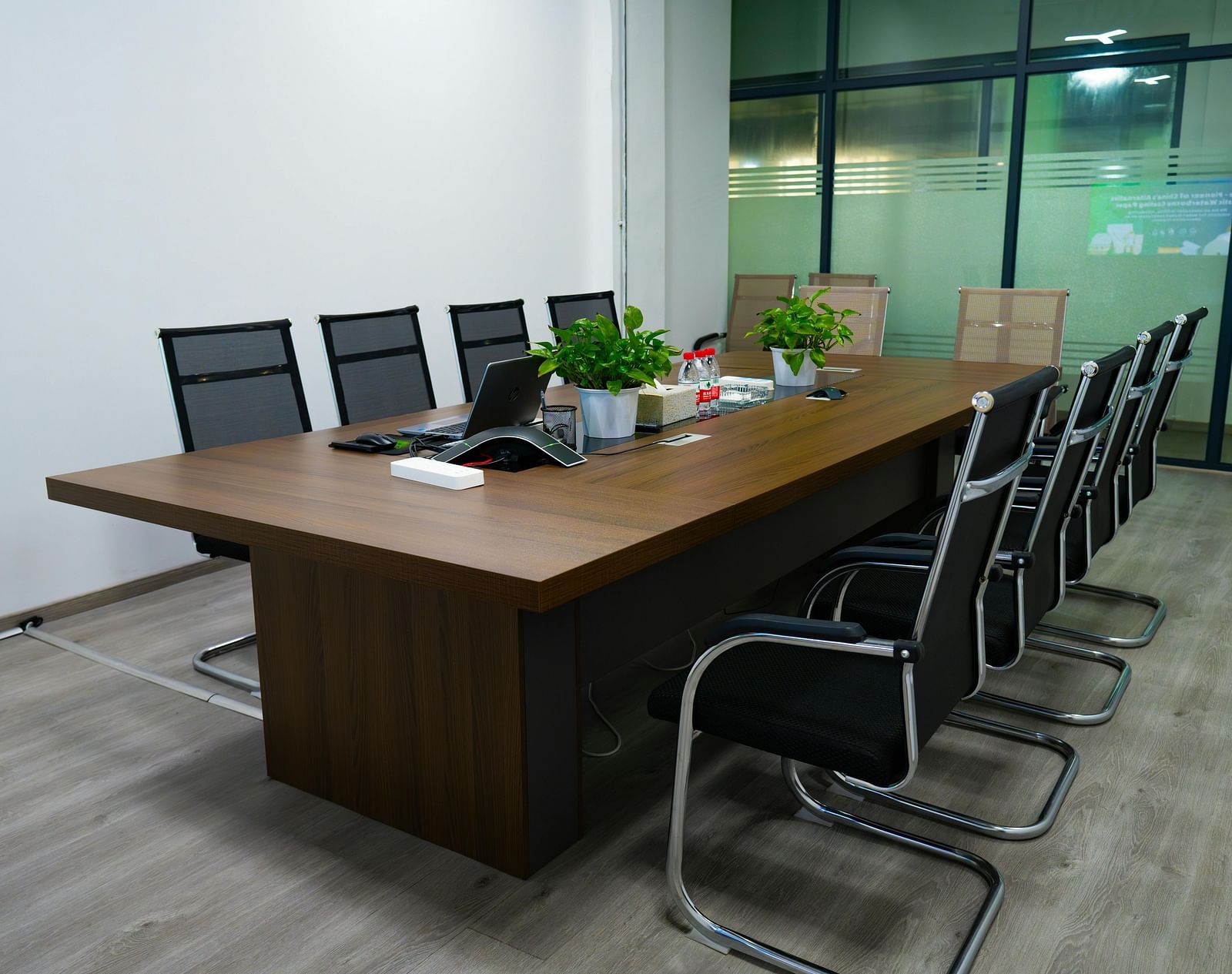 Corner view of a boardroom with a wide wooden table along with several chairs surrounding it.