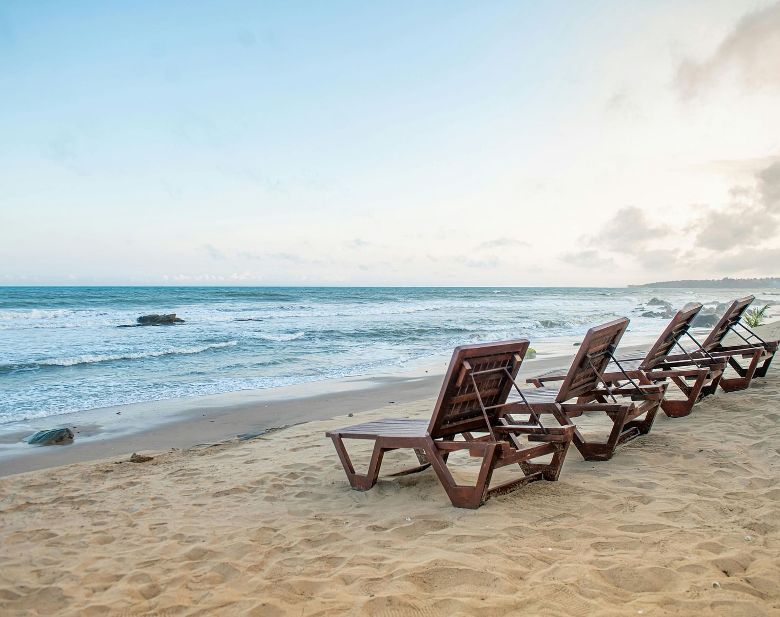 Wooden loungers placed in front of a shoreline on the beach during the day.
