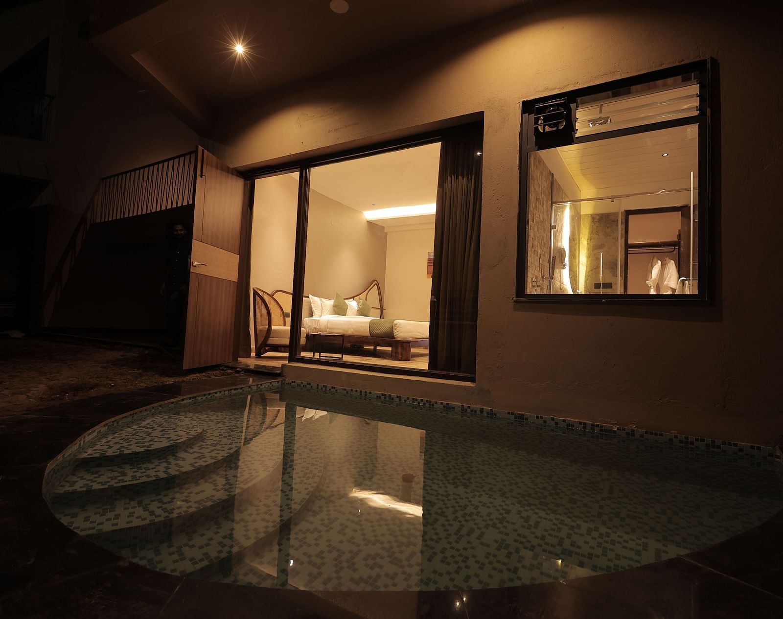 Luxury Villa with Plunge Pool featuring an outdoor pool area at night, with ambient lighting and seating visible through glass windows at The Qualia Resort Club & Brewery, Udaipur.