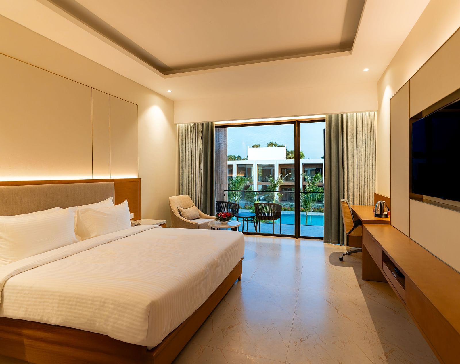 A hotel room at The Shore Trishvam, Pondicherry featuring a double size bed, flat TV screen, and a balcony arranged with two chairs. 