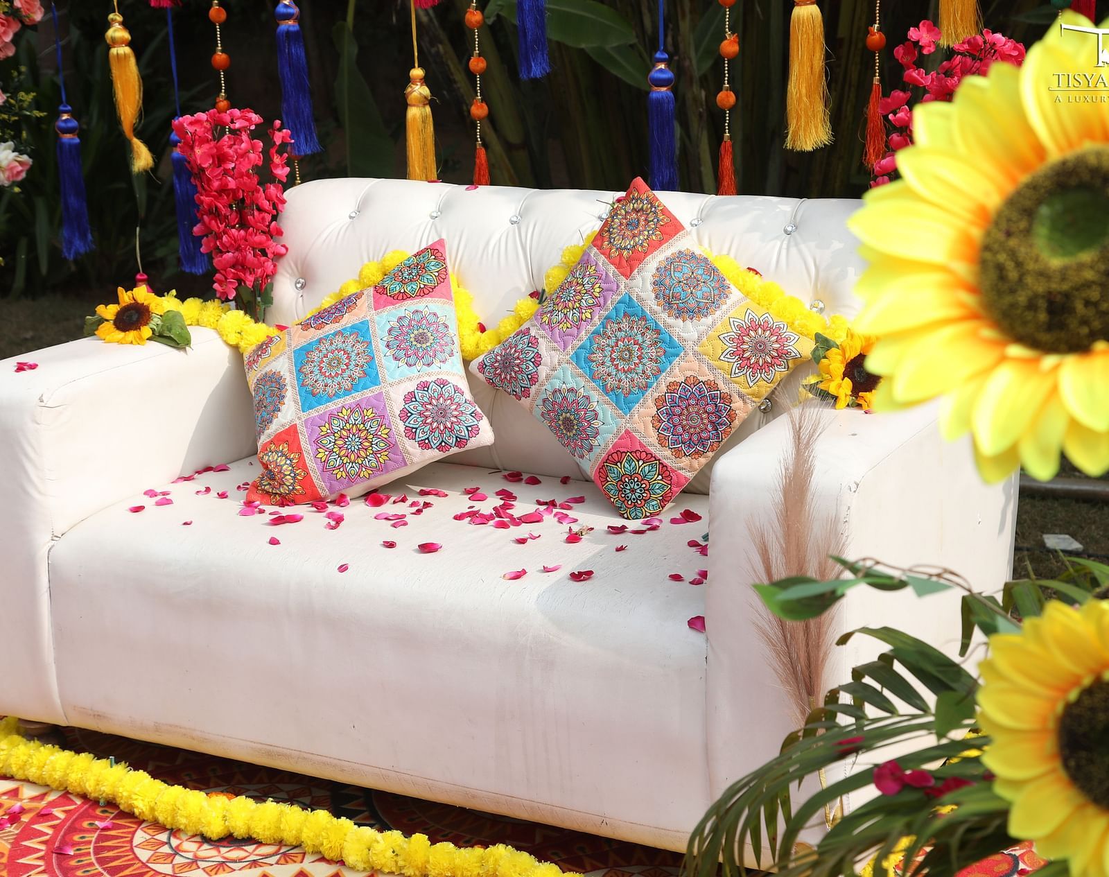 A white sofa adorned with colourful cushions and surrounded by sunflower decorations, placed on a vibrant rug at Tisya Farms.