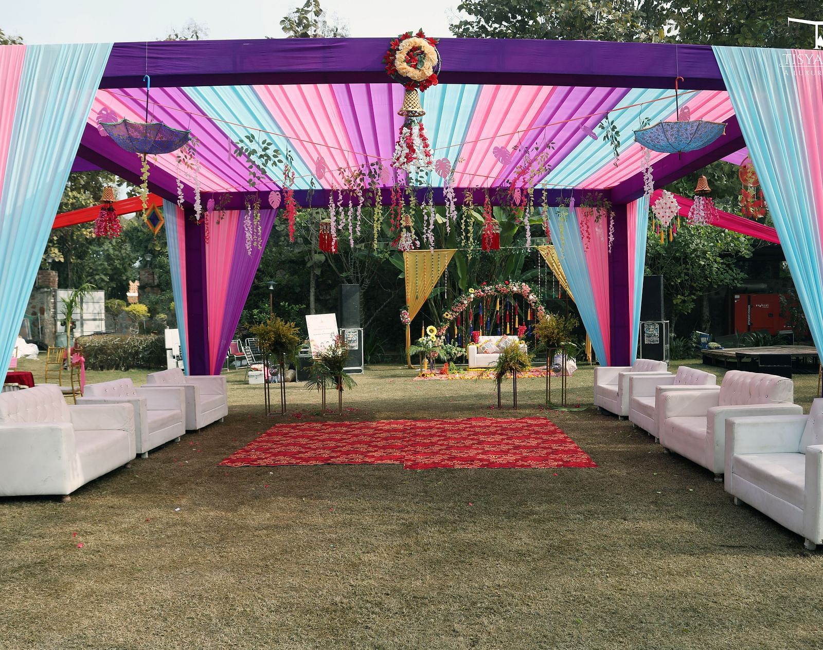 A beautifully decorated outdoor canopy with pink, purple, and blue drapes, featuring white seating arrangements for guests at Tisya Farms.