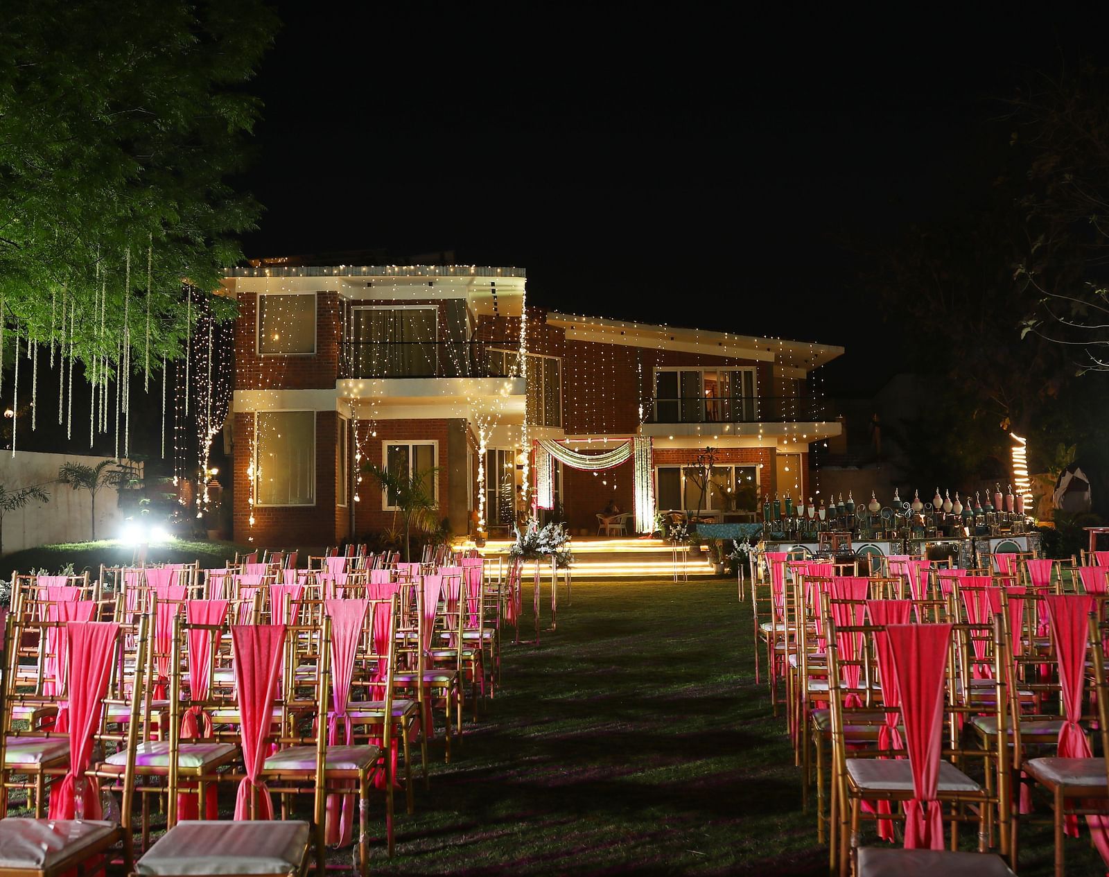 Outdoor event setup at Tisya Farms, Gurgaon with rows of red chairs facing the lit-up main building at night.