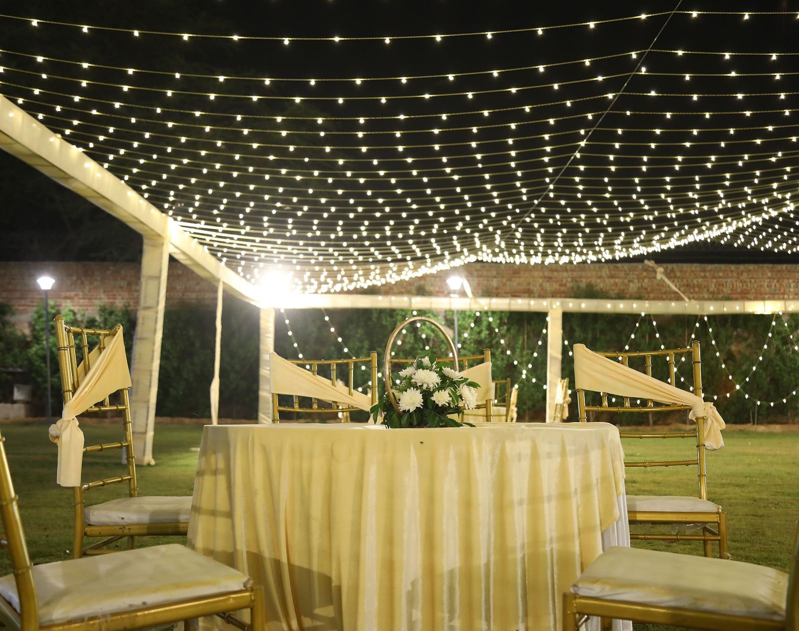 Outdoor table setup at Tisya Farms, Gurgaon under a canopy of hanging string lights.