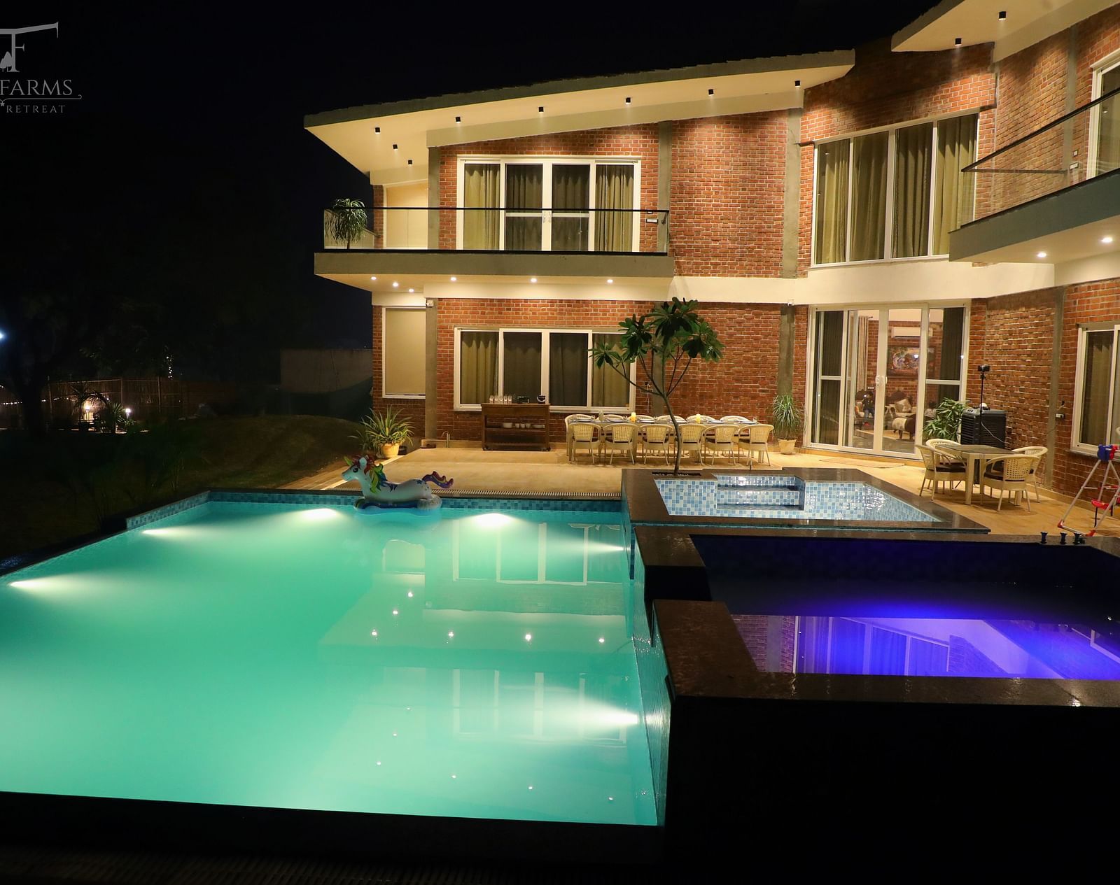 A night view of a farmhouse with an illuminated swimming pool in front at Tisya Farms, Gurgaon.