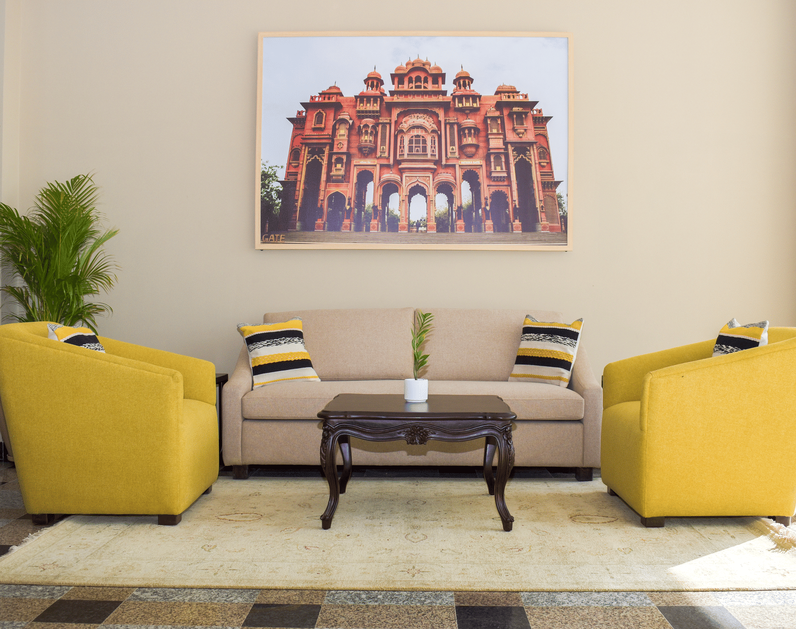 A hotel lobby seating area with yellow armchairs, a beige sofa, a dark wood coffee table, a framed image of a building, and a potted plant at our Hotel Near JECC - Urban Suites by BluSalzz, Jaipur
