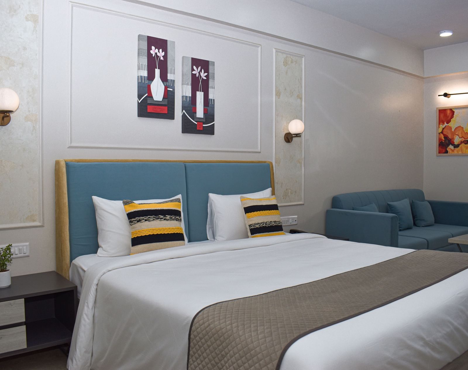 A Budget Hotel in Jaipur's room with a bed, a blue sofa, a small table, wall-mounted light fixtures, and framed artworks - Urban Suites by BluSalzz, Jaipur