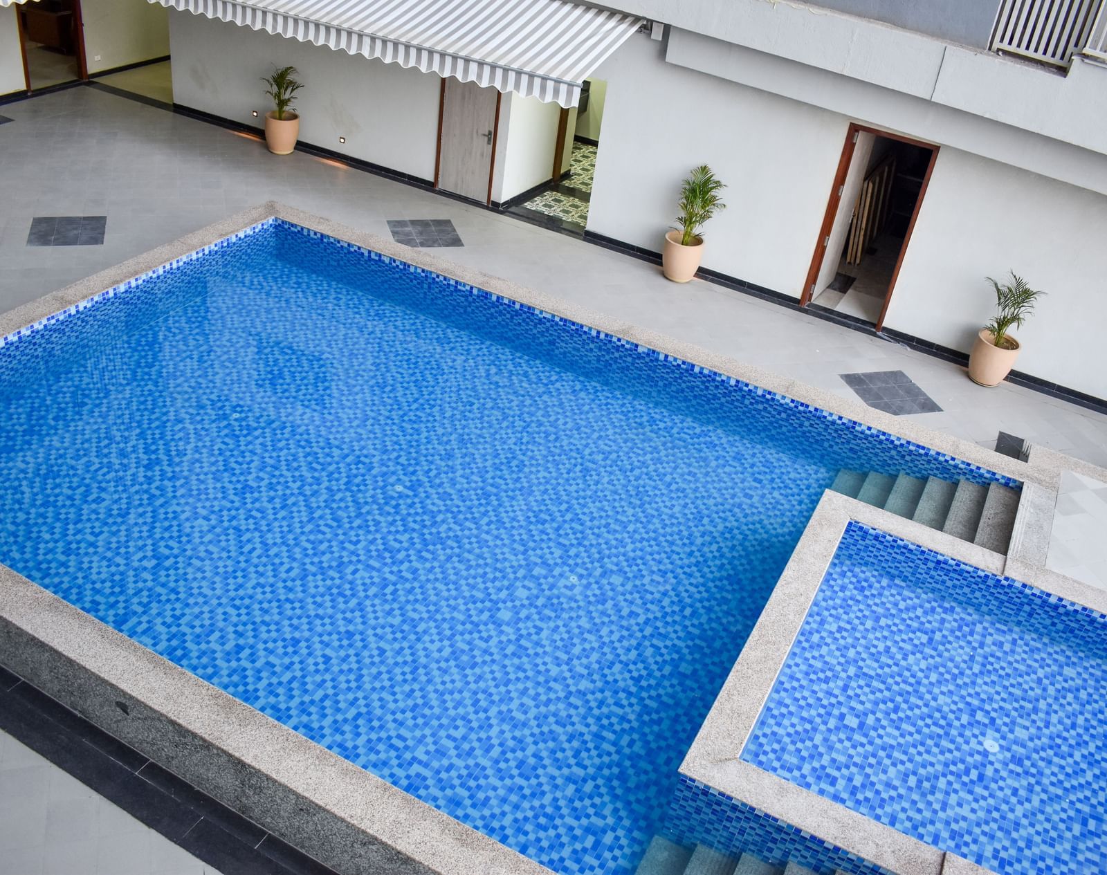 An outdoor swimming pool with blue tiles, surrounded by a concrete patio, potted plants, and building exteriors - Urban Suites by BluSalzz, Jaipur