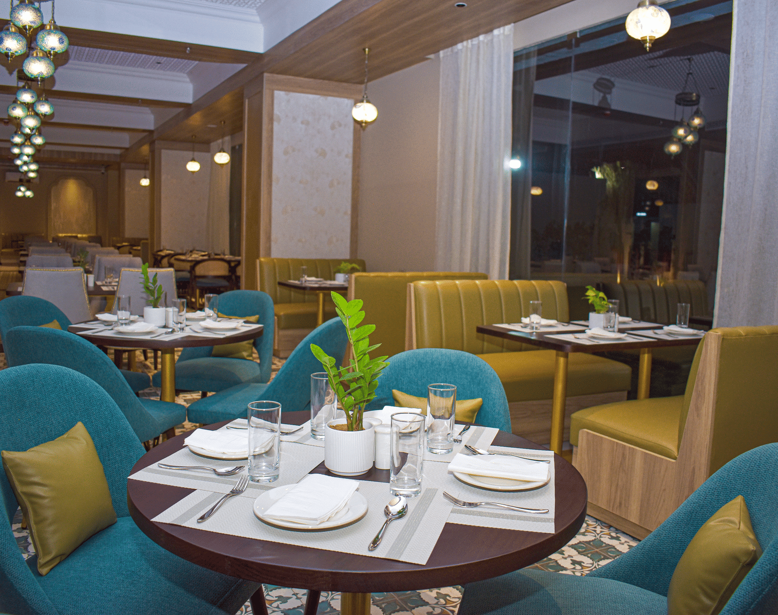 A restaurant interior with armchairs, booth seating, round tables, a patterned floor, sheer curtains, and hanging pendant lights - Urban Suites by BluSalzz, Jaipur