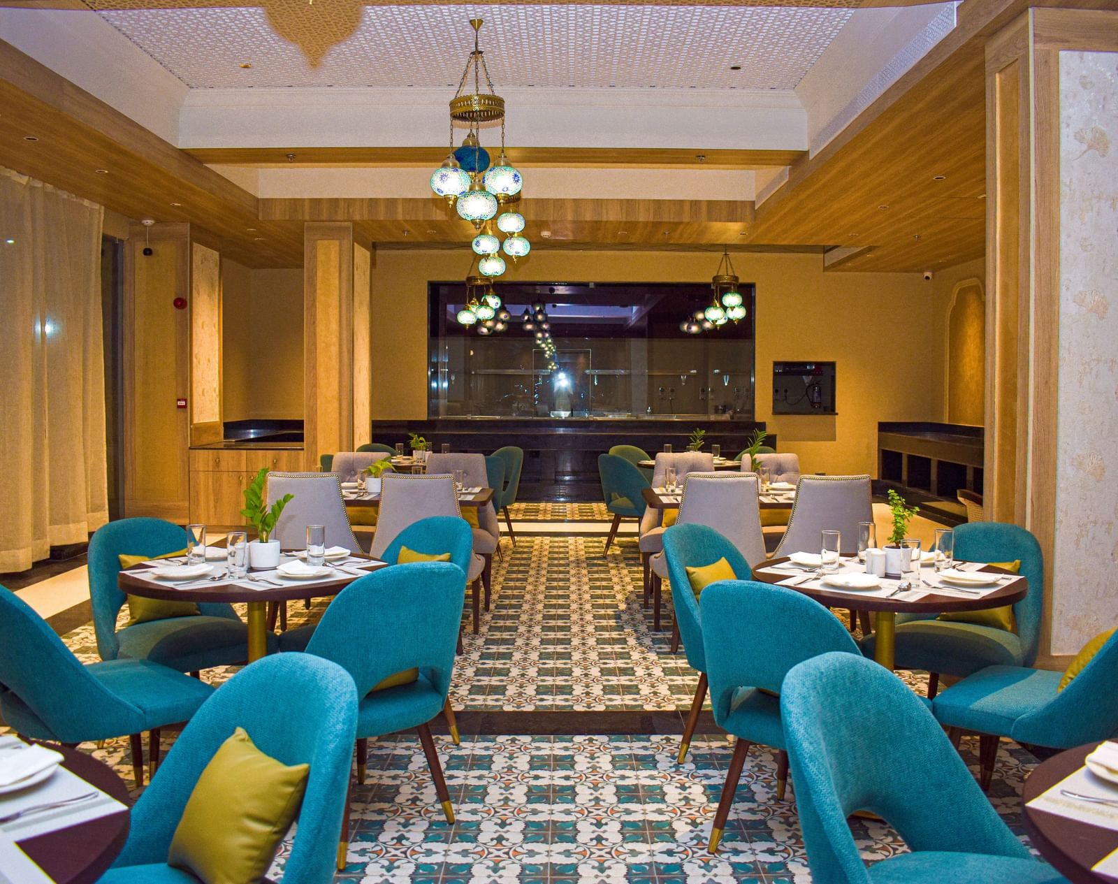 A modern restaurant interior with teal armchairs, round tables, patterned tile floor, and a distinctive globe chandelier - Urban Suites by BluSalzz, Jaipur