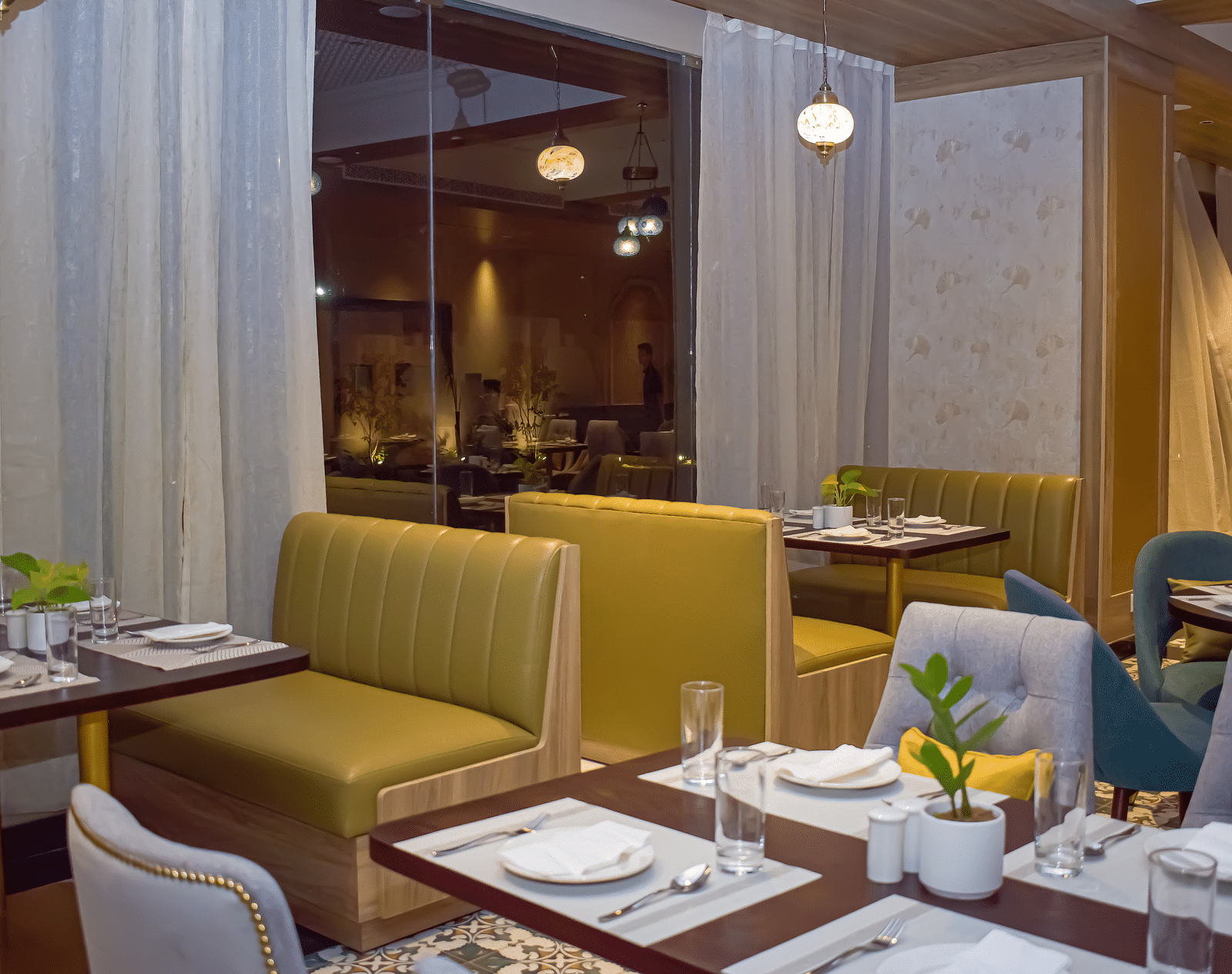 A restaurant interior with booth seating, set tables, sheer curtains, and hanging pendant lights - Urban Suites by BluSalzz, Jaipur