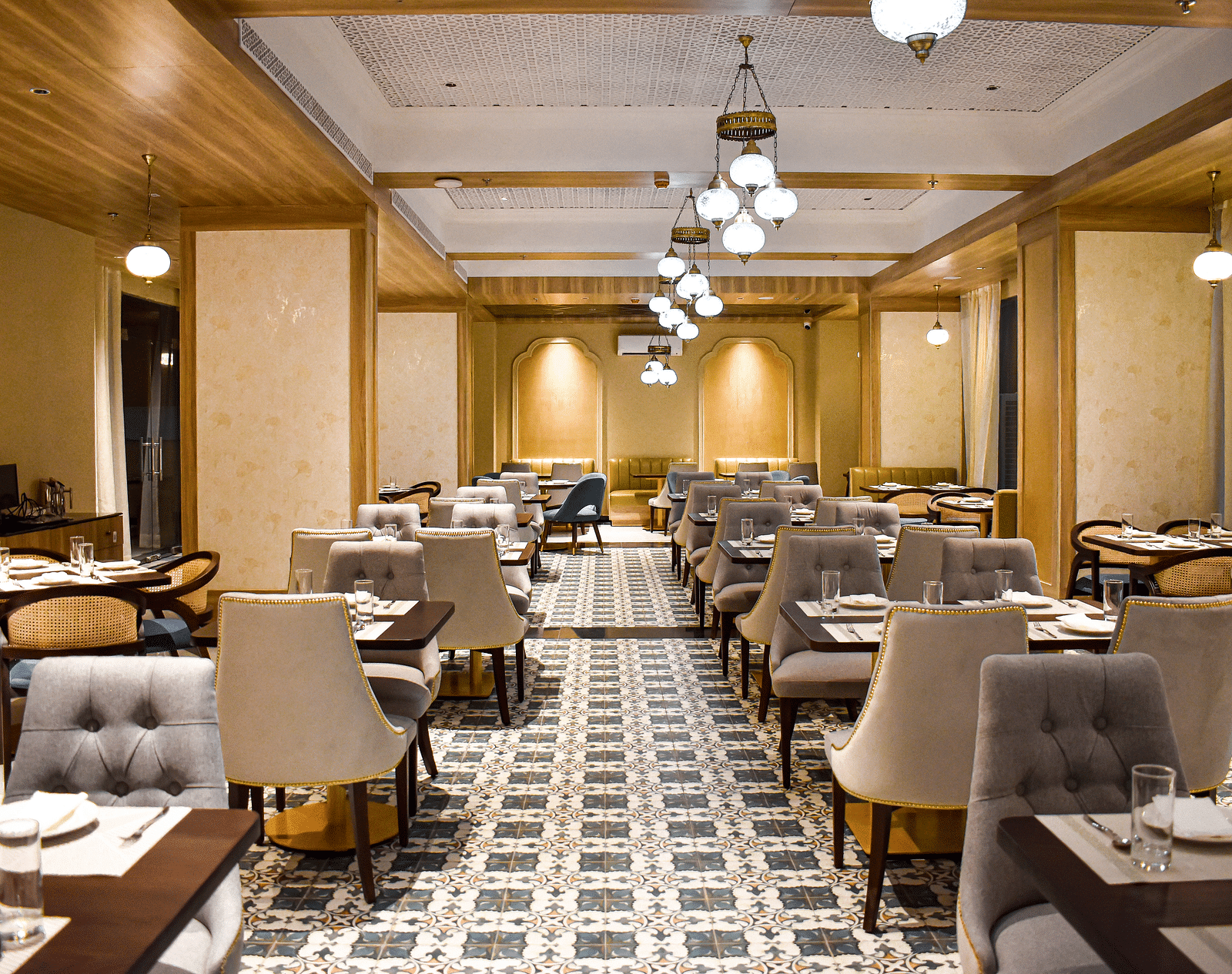 A restaurant interior with patterned tile floor, upholstered chairs, set tables, hanging pendant lights, and decorative ceiling panels - Urban Suites by BluSalzz, Jaipur